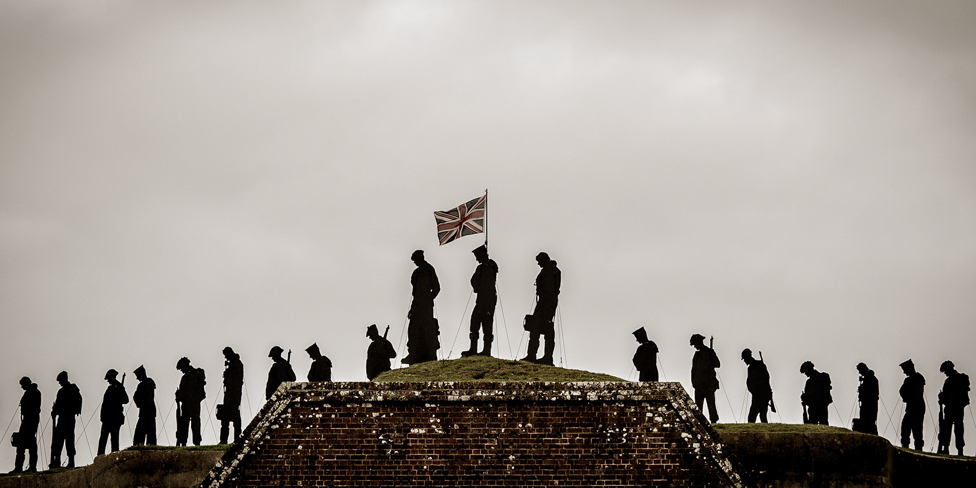 As the Union Jack ripples in a breezy autumnal sky, a row of stark silhouettes of fallen soldiers stand against the fading light, a silent and powerful tribute on Armistice Day