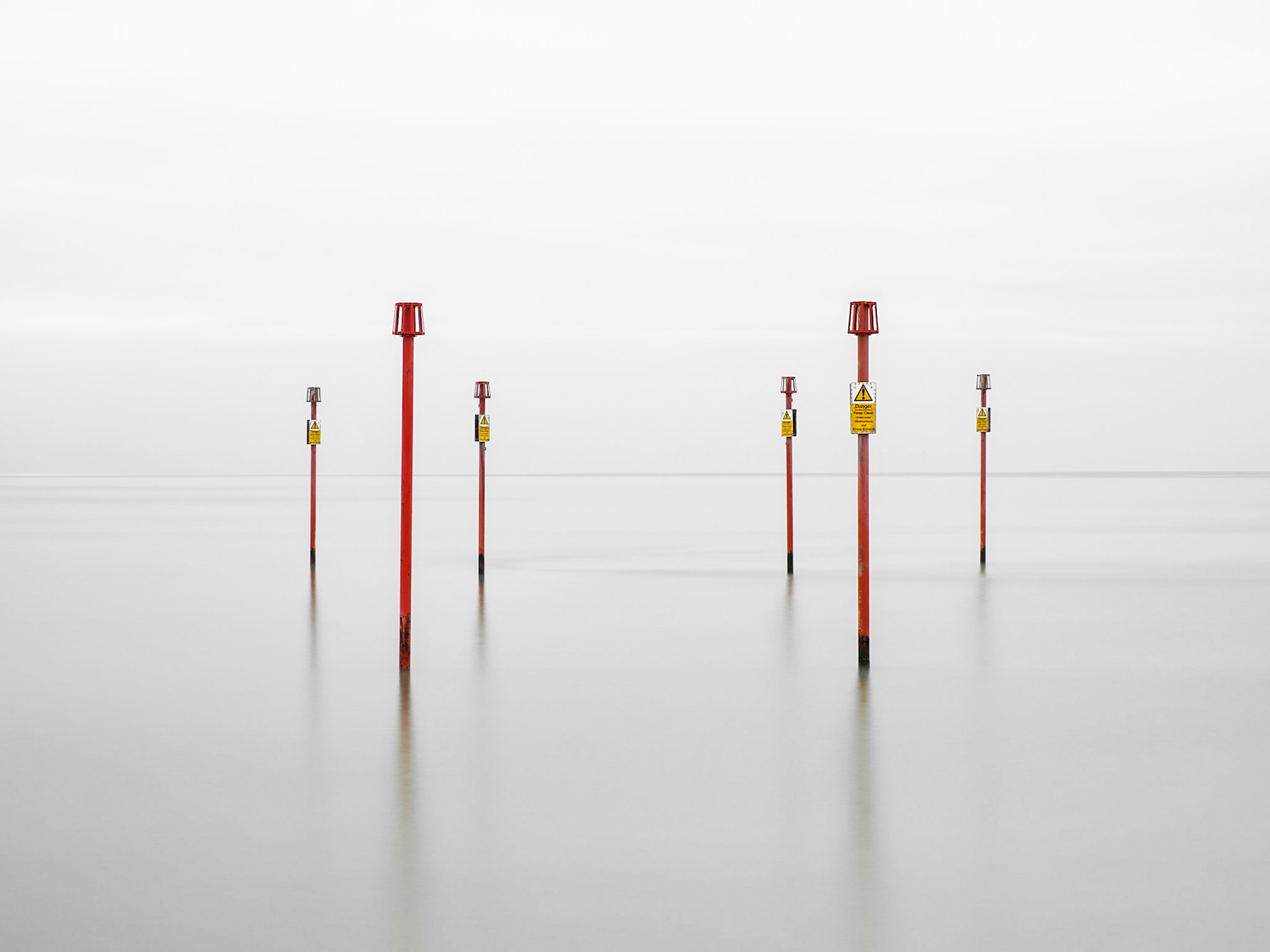 Marker poles stand out on a perfectly calm but misty sea on the south coast of England