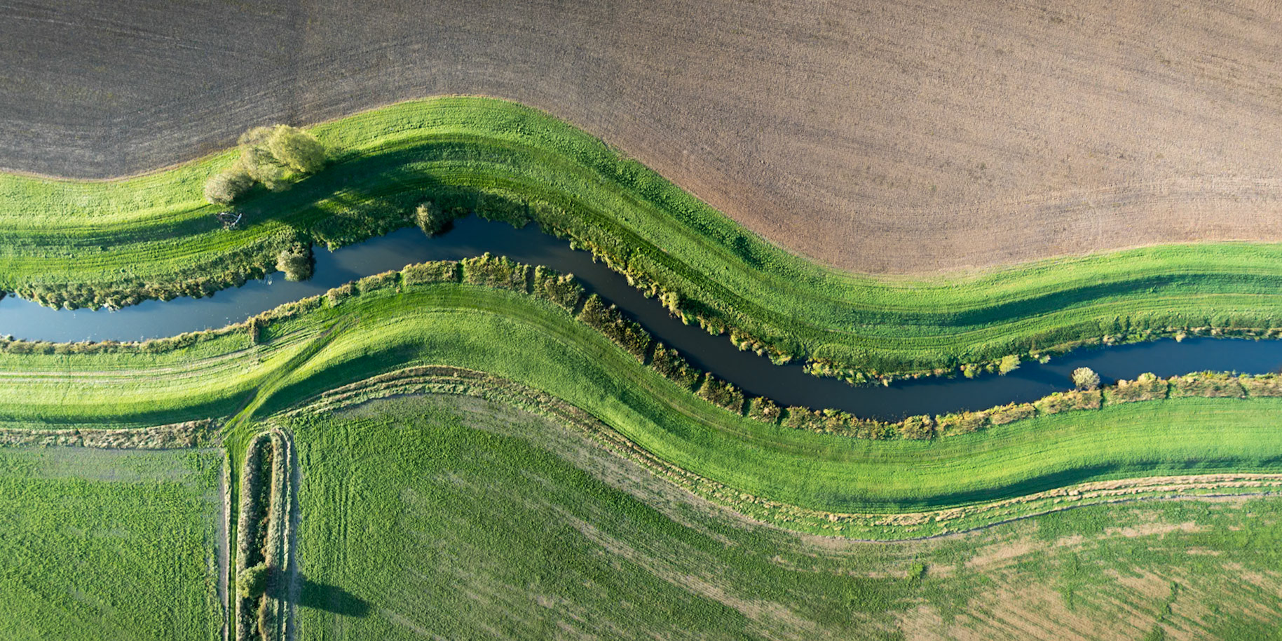 A low sun casts shadows across the grassy banks of the River Rother in Sussex