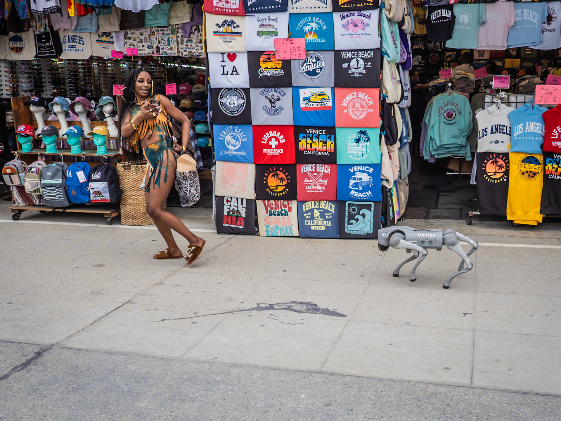 A woman runs away from a robotic dog chasing her along the boardwalk of Venice Beach in California