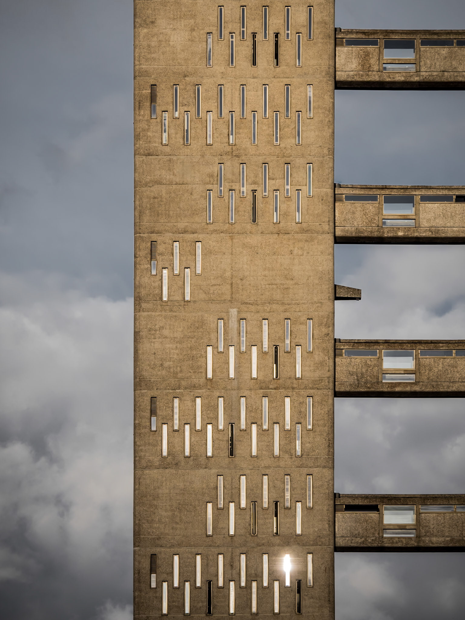 The setting sun reflects off one of the multitude of slit windows of the service tower of Balfron Tower in East London