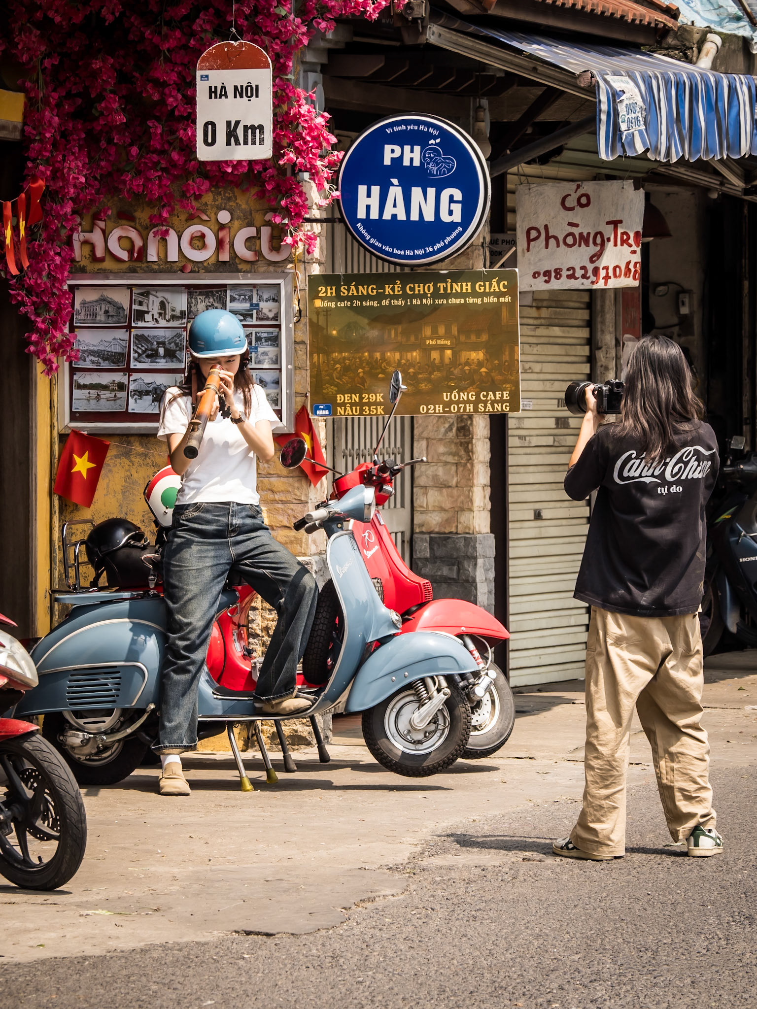 A young woman poses with a pair of vintage mopeds for a photoshoot on a back street in Hanoi