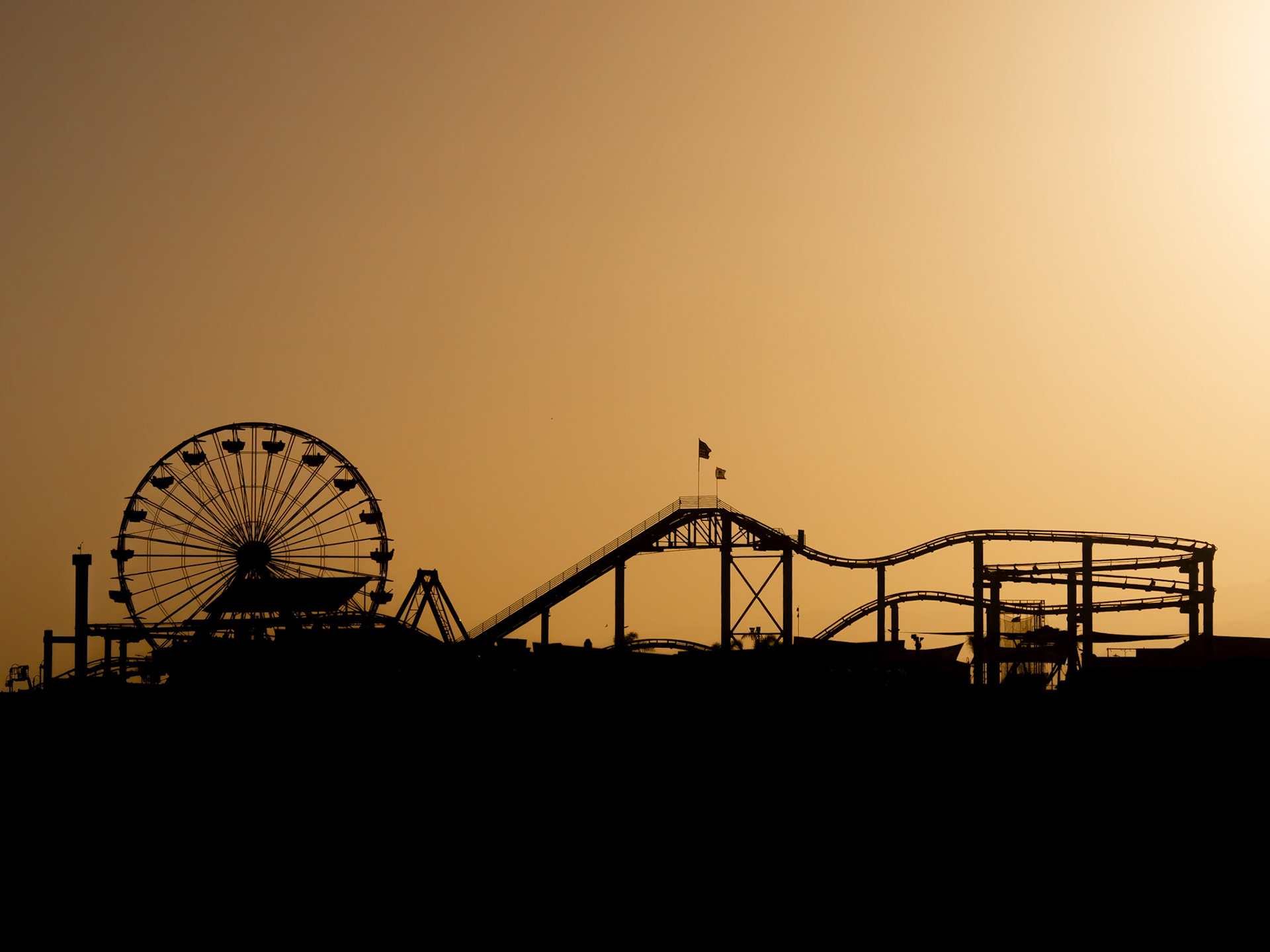 The sun sets behind the funfair on Santa Monica Pier in California