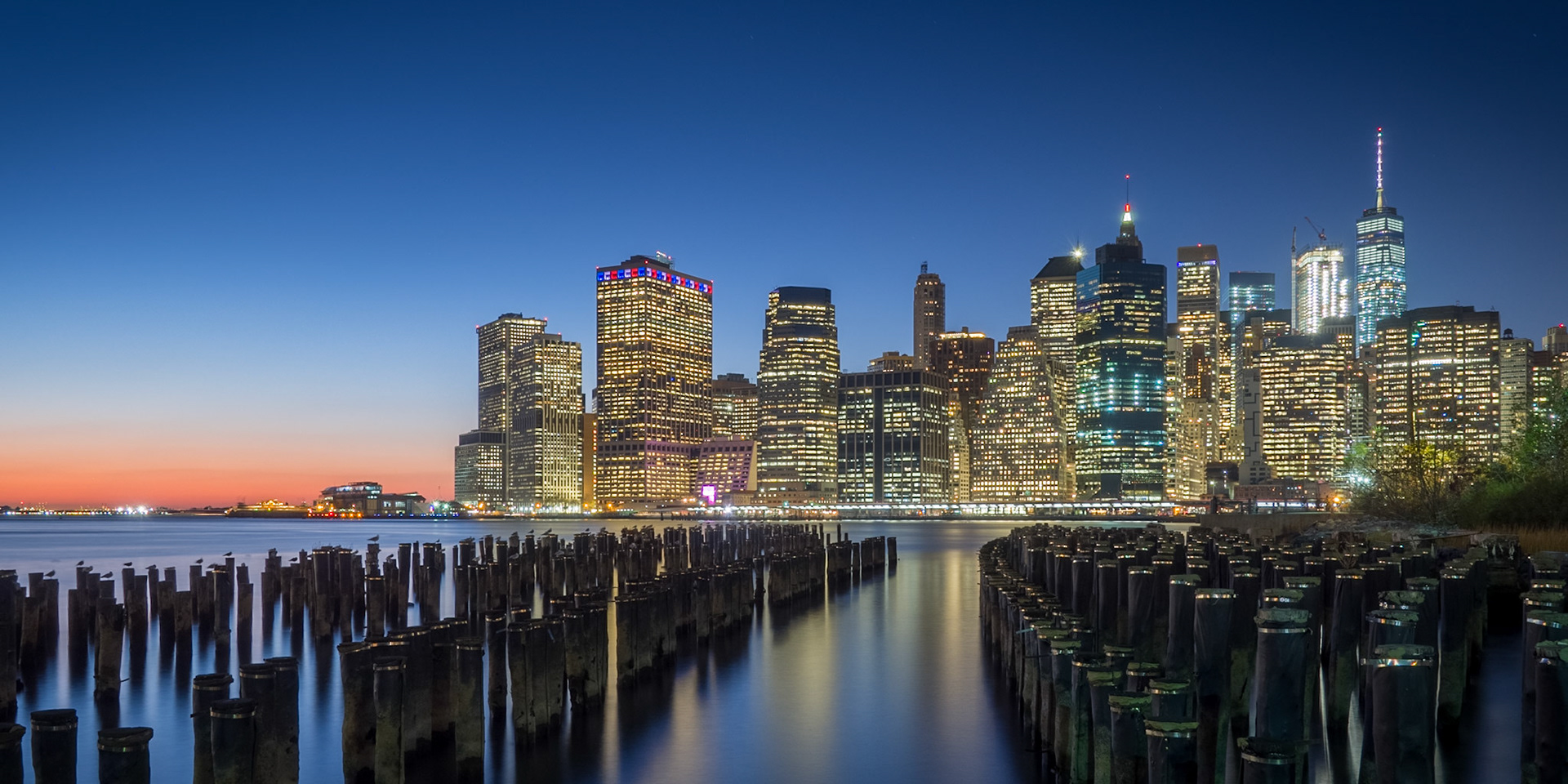 The lights of Lower Manhattan sit behind the remains of dock pilings in Brooklyn, New York