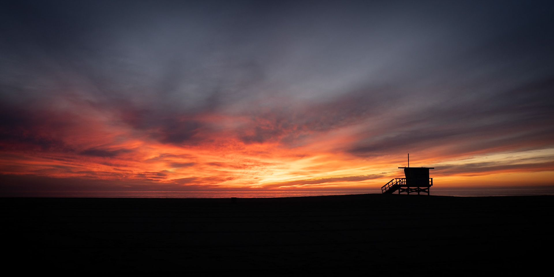 A life guard station on Venice Beach lies empty as a vibrant sun sets over the Pacafic Ocean