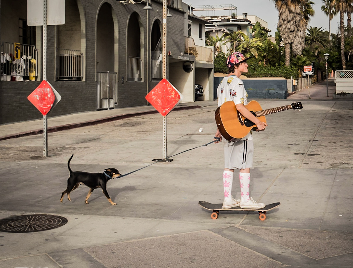 A dog trails behind his musician owner along the beachfront in Venice, California
