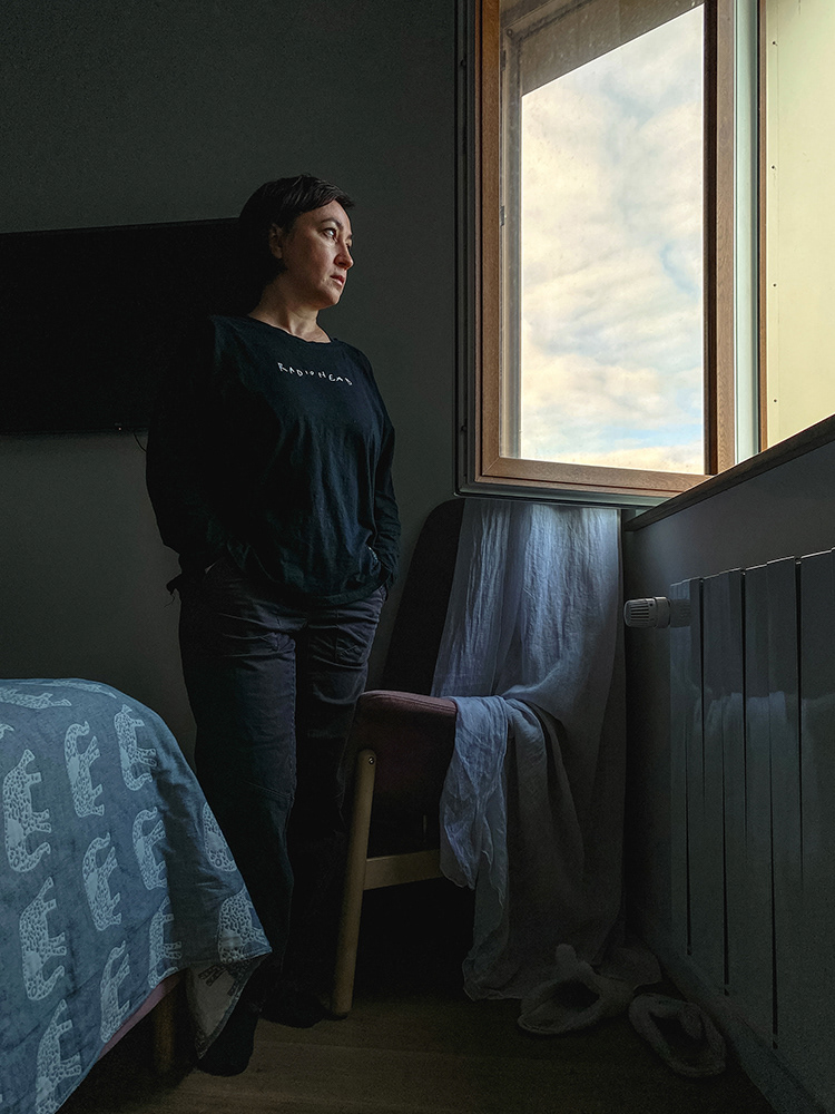 Eine Frau steht in einem Raum und blickt aus einem offenen Fenster, Porträt von Oxana Guryanova