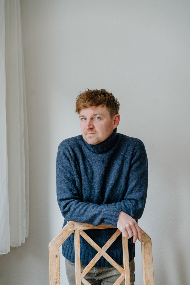 Porträt eines Mannes im blauen Pullover auf Holzstuhl, von Dokumentarfotografin Oxana Guryanova.