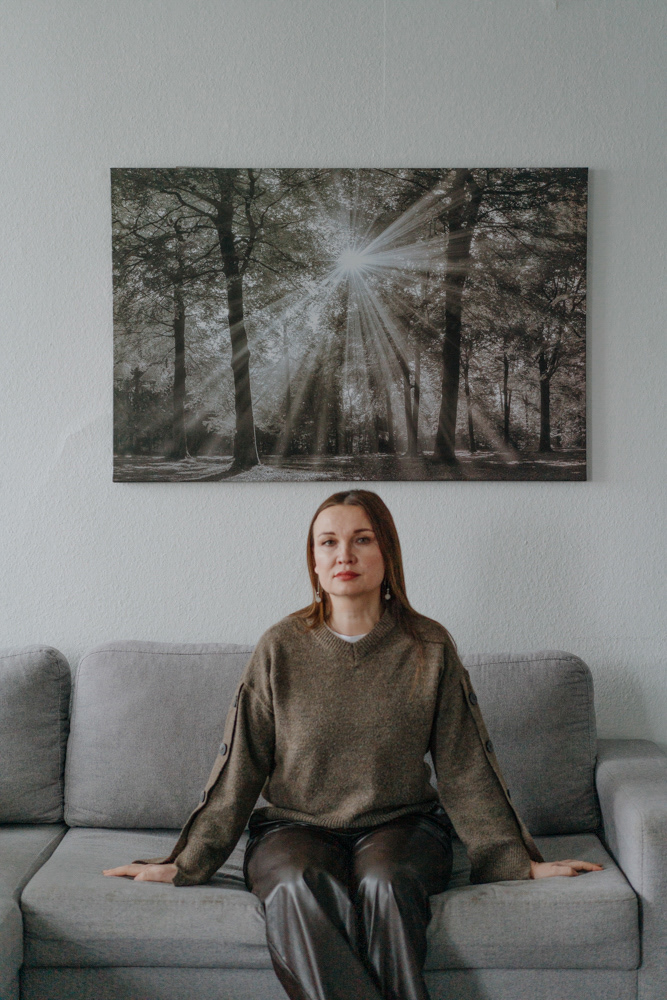 Frau auf grauem Sofa sitzend, Porträt von Dokumentarfotografin Oxana Guryanova.