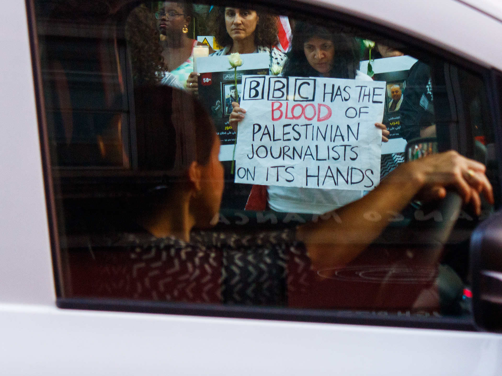 August 13th, 2025 - A car driver looks at a placard that is being held by a protester