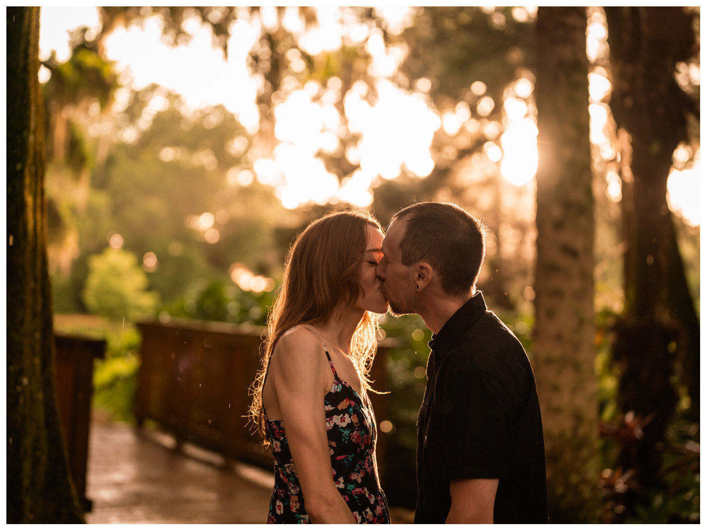 Couple kissing beside a wooden walkway in golden light at Washington Oaks Gardens State Park.
