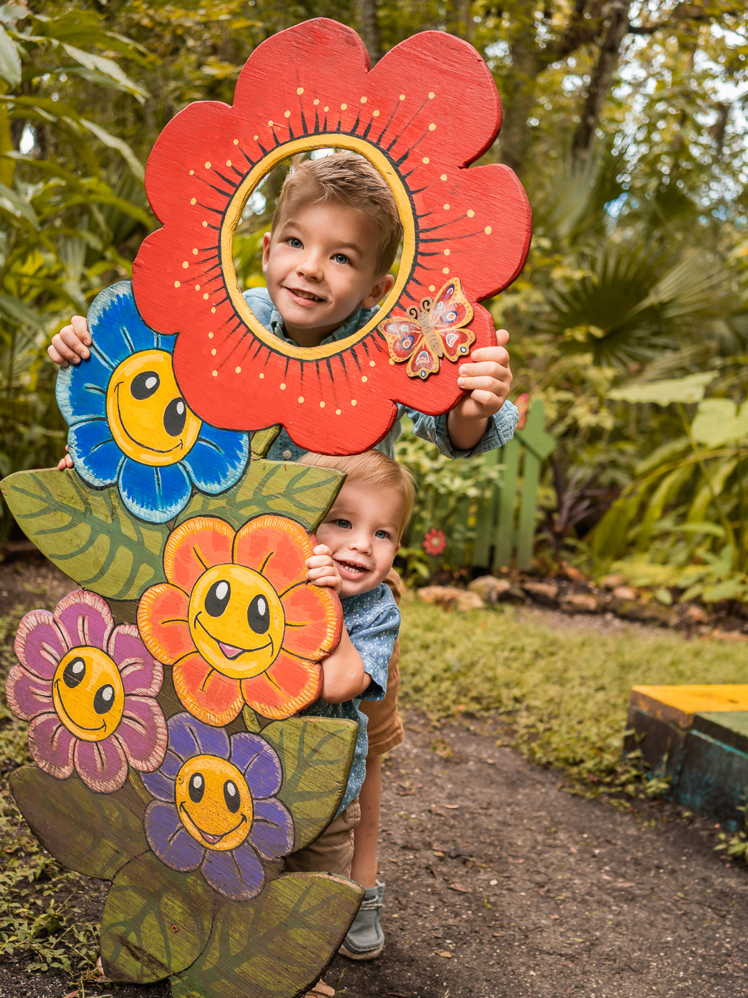 Little boy peeking through a flower-shaped cutout during playful family portraits in Dunlawton Sugar Mill Gardens.
