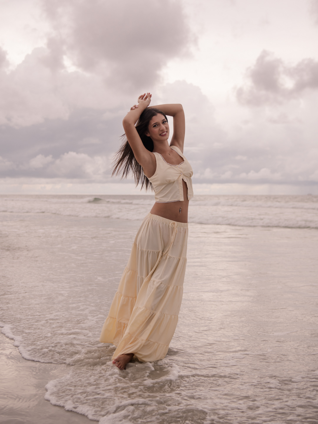 Senior photos at Daytona Beach, Mia playing in the ocean waves in a cream dress, joyful and candid portrait.