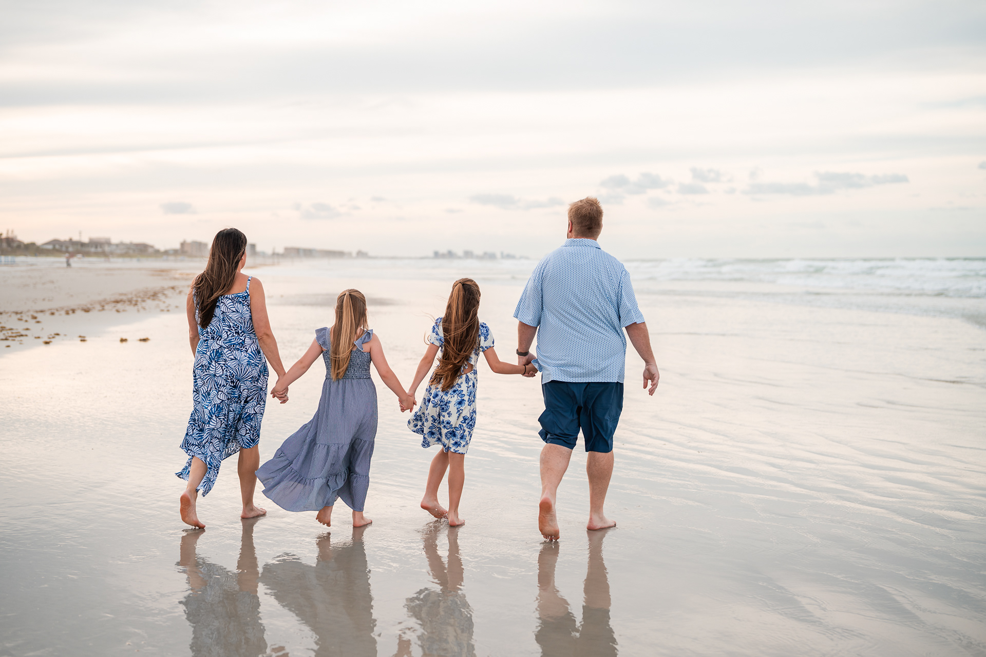 Family walking hand in hand along the shoreline during a Ponce Inlet Beach photo session.