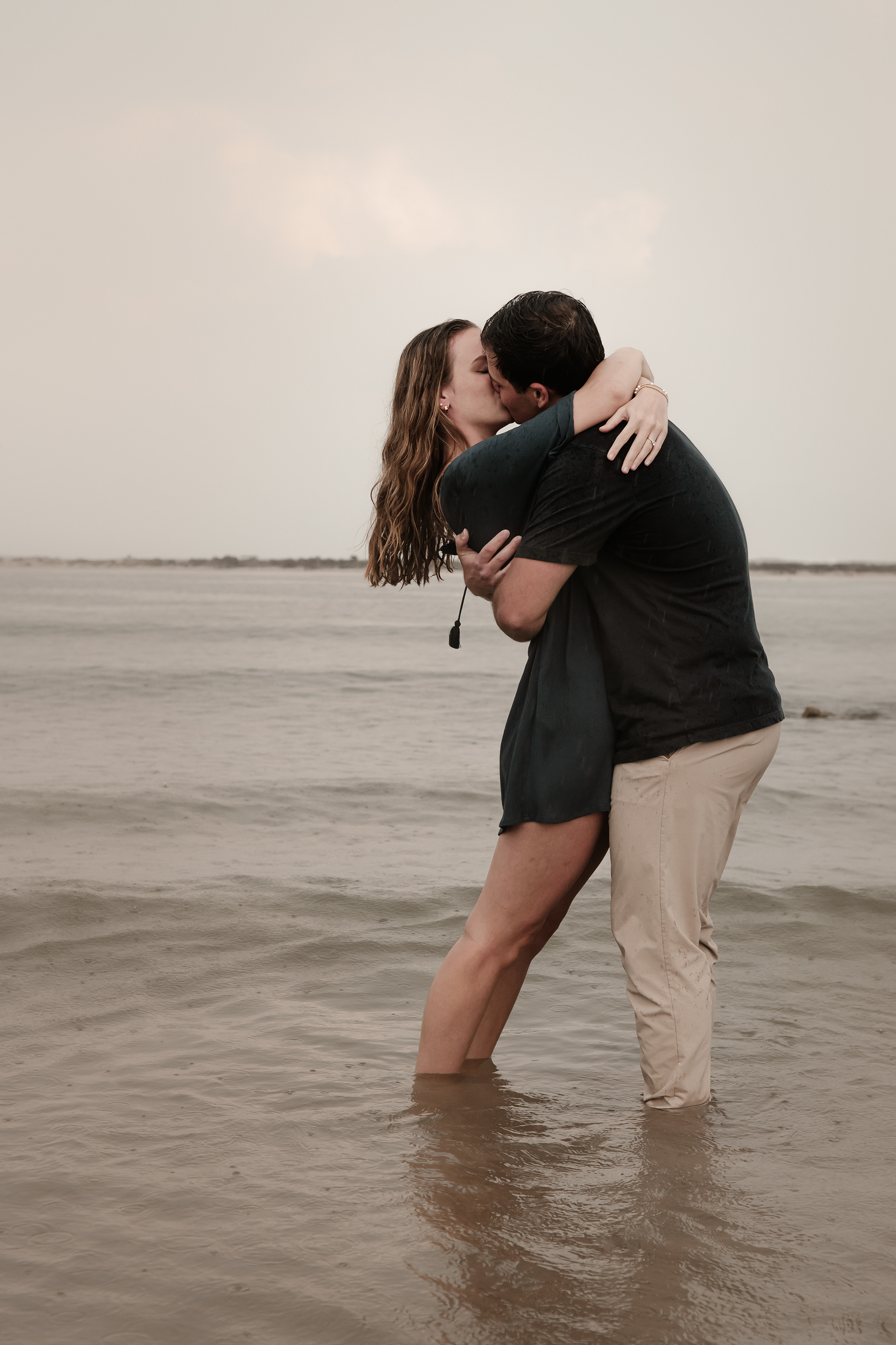 Rainy Ponce Inlet engagement photo of couple kissing in shallow water during beach session