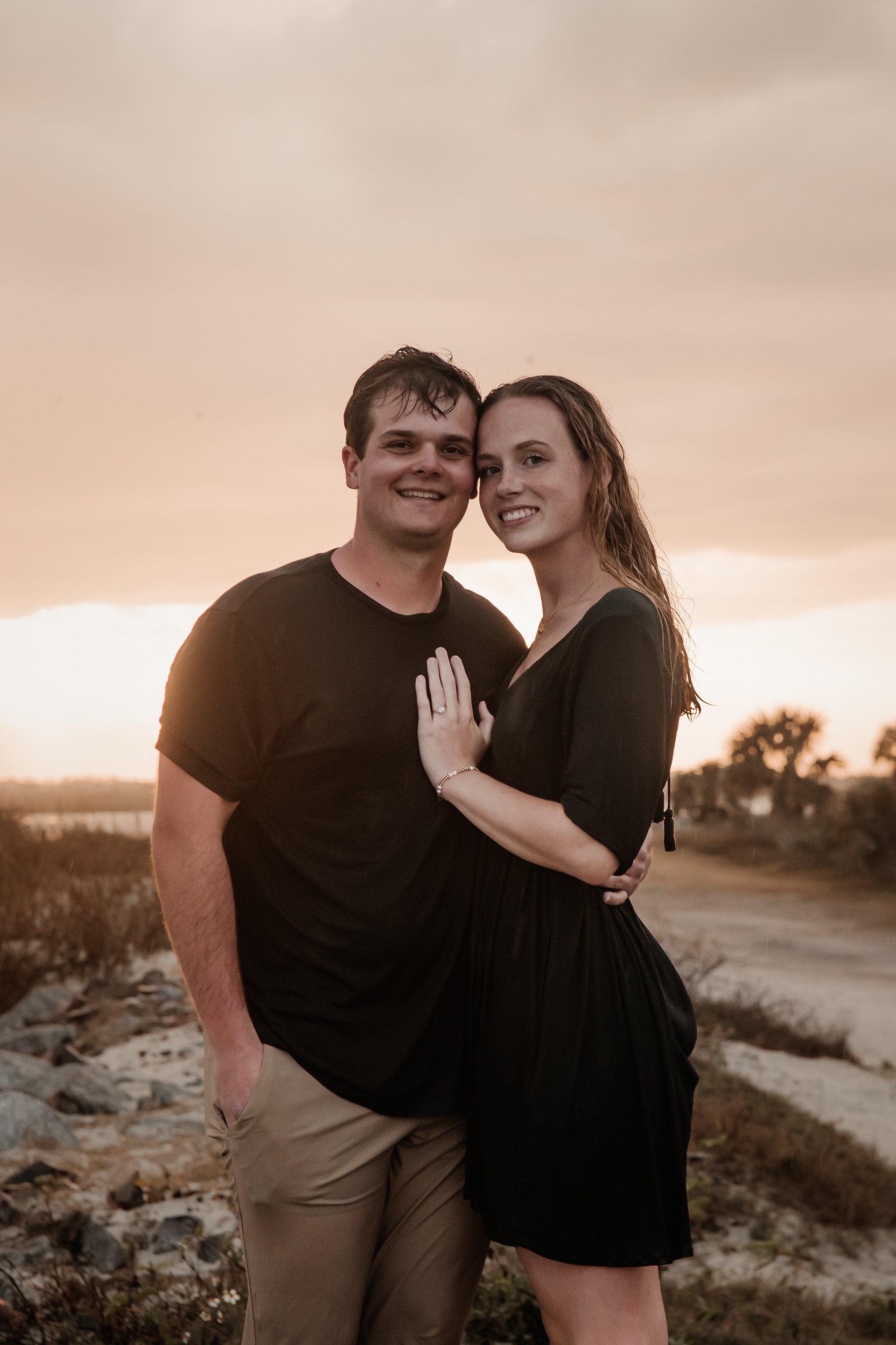 Ponce Inlet beach engagement portrait with couple standing near rocks and sunset sky