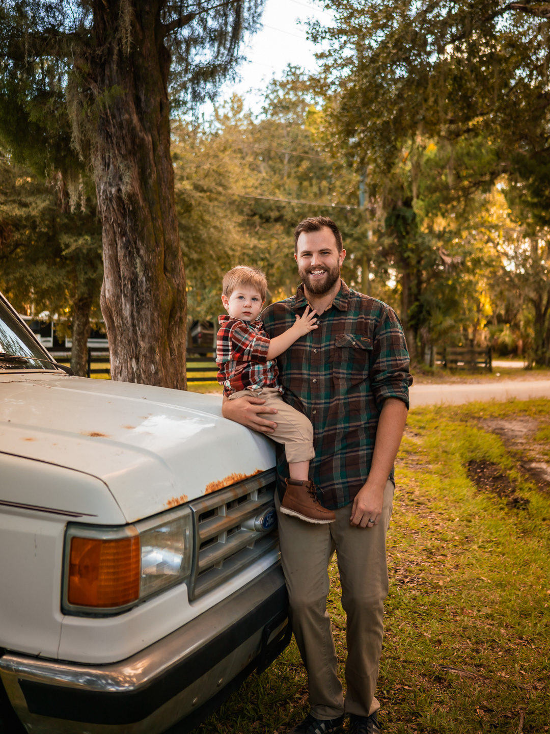 Family standing by vintage truck with their young son and dog during golden-hour backyard photos in New Smyrna Beach.