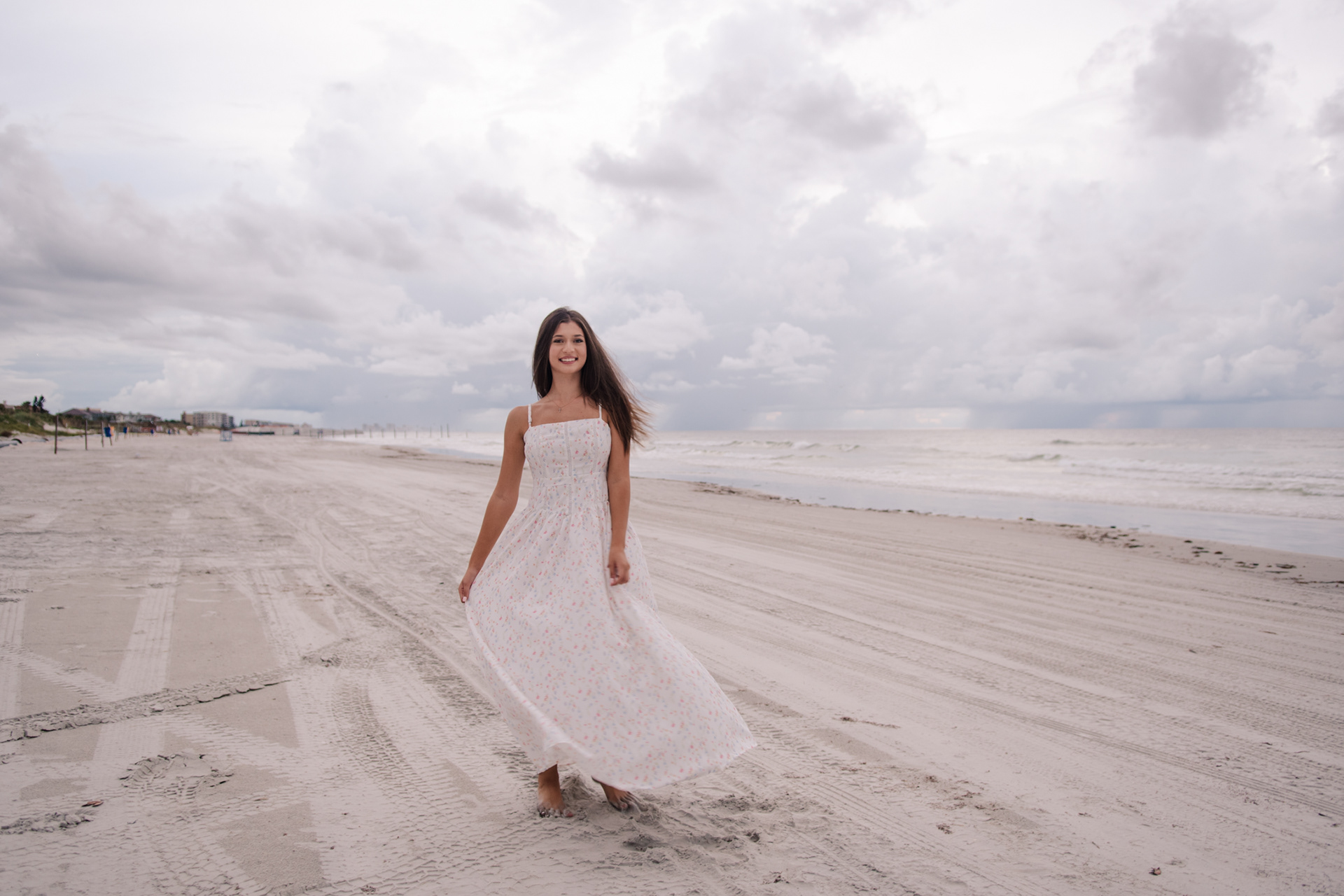 Senior portraits in Daytona Beach area, Mia walking along the shoreline in a flowing white floral dress.