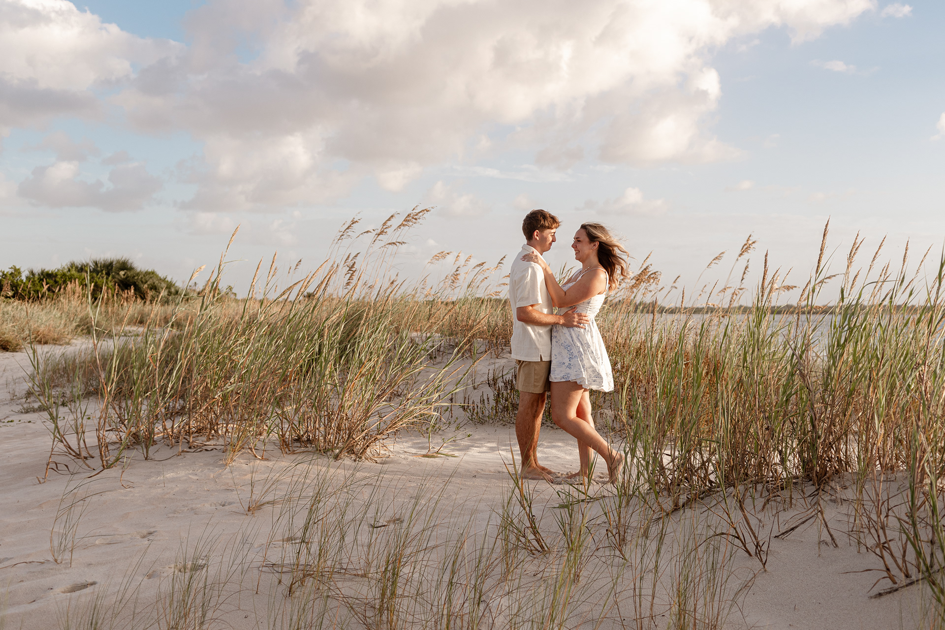 Couple walking through sea oats during sunset engagement session at New Smyrna Beach.