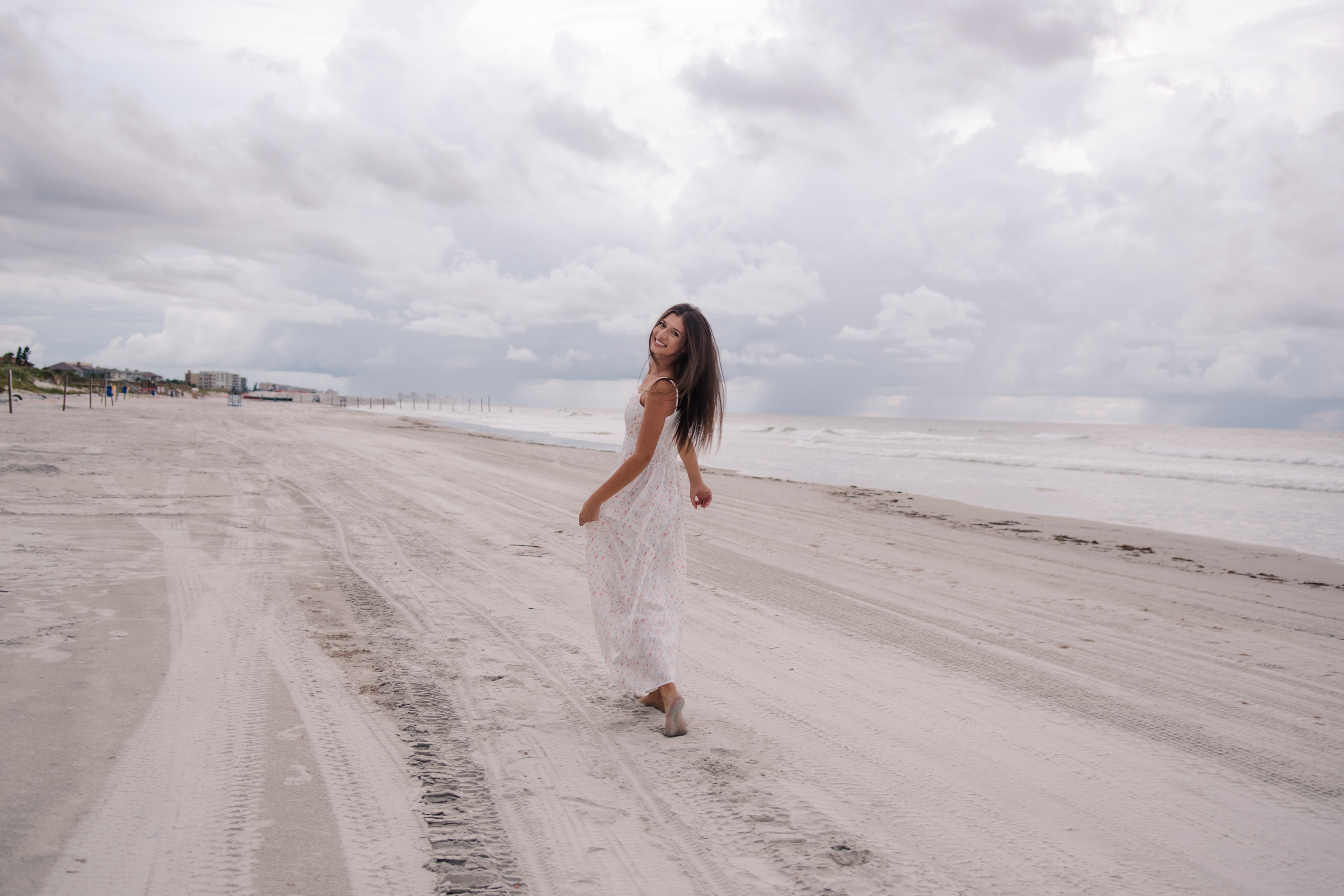 Daytona Beach senior portraits, Mia walking along the shoreline in a white floral dress, candid beach moment.