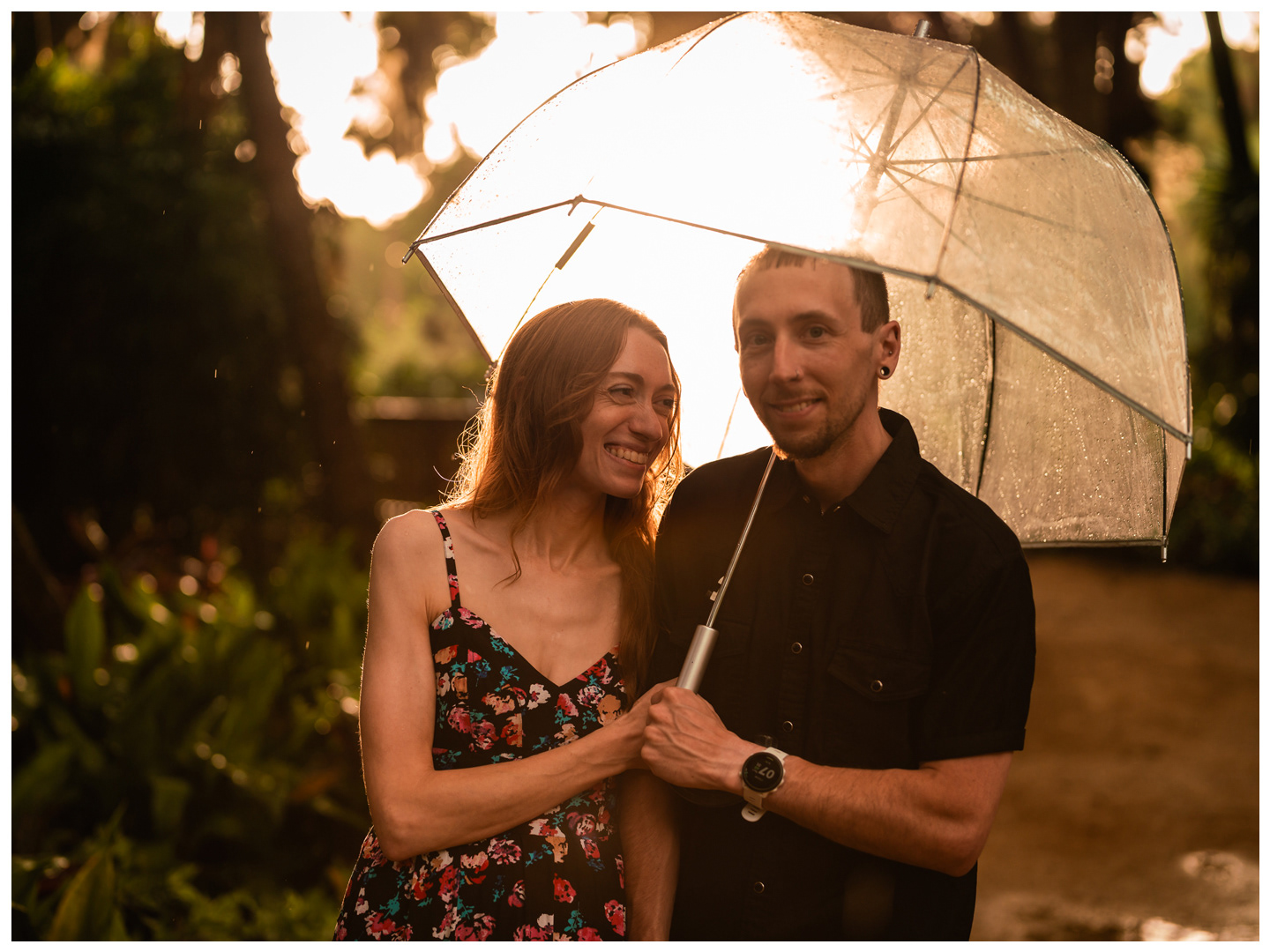 Couple laughing together beneath a clear umbrella on a rain-soaked path at Washington Oaks Gardens State Park.