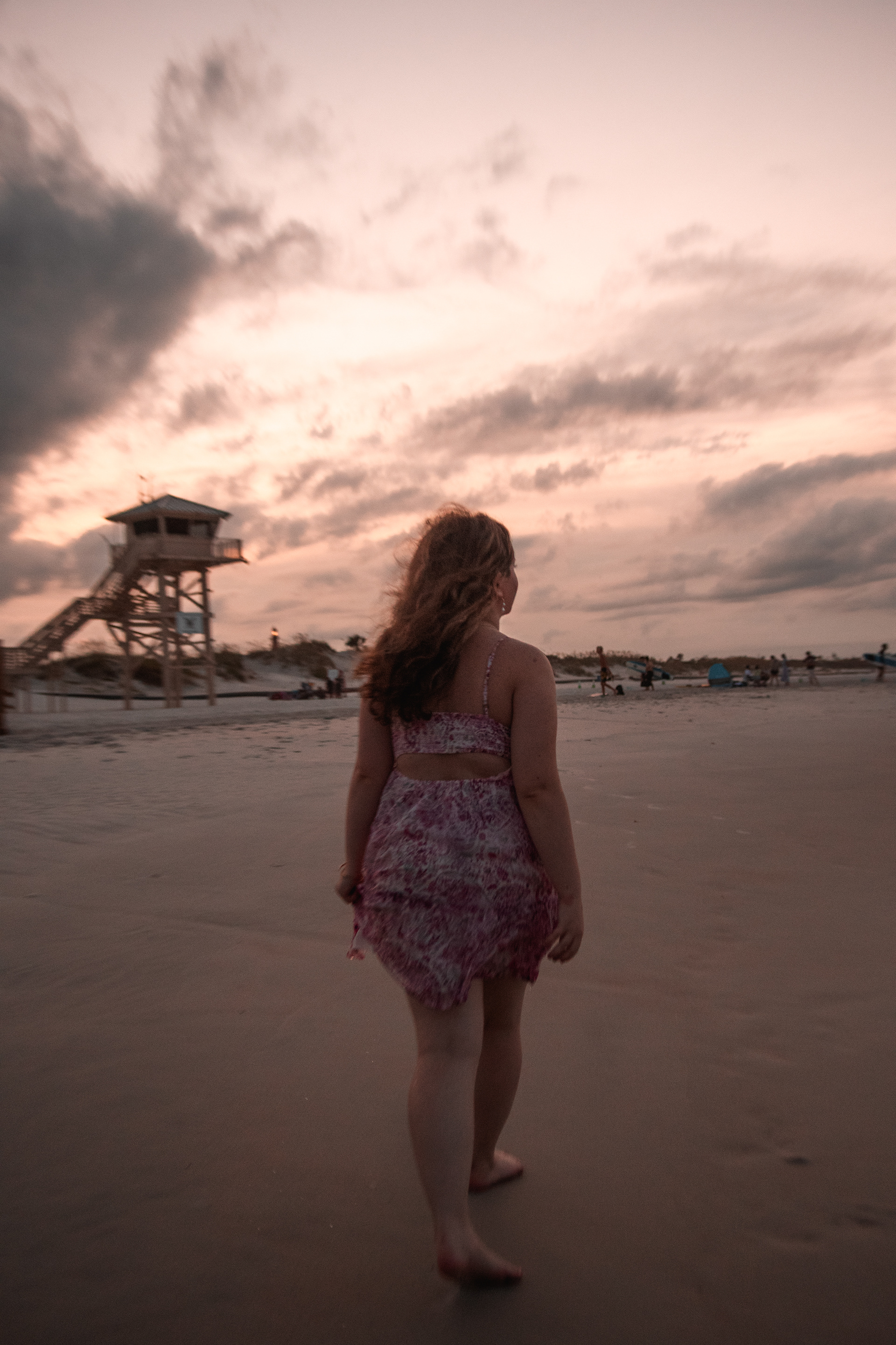 Senior photos in Ponce Inlet FL, Nelly walking toward the shoreline rocks with golden sunset sky overhead.