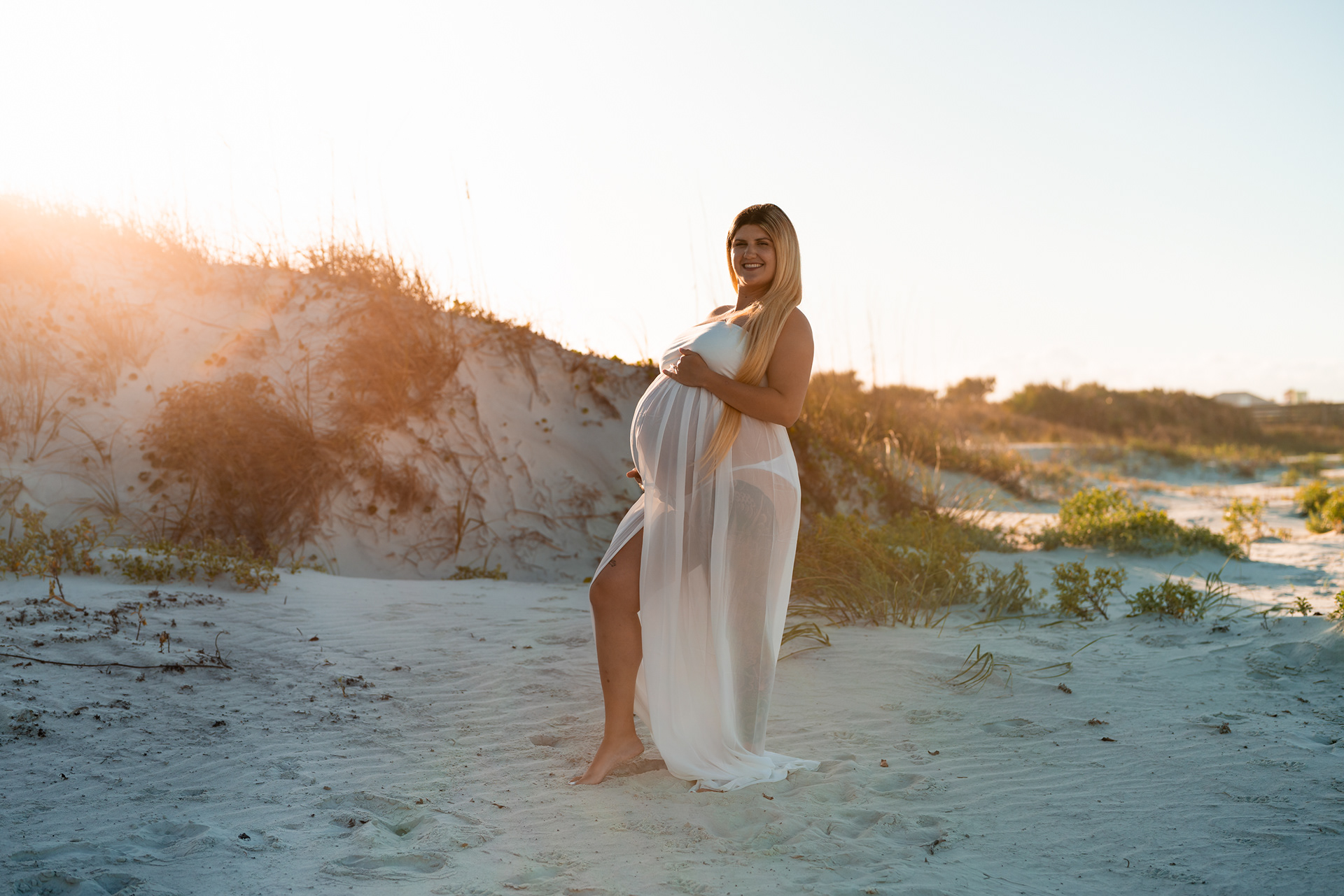 Beach maternity photo in white dress standing by the dunes in Florida