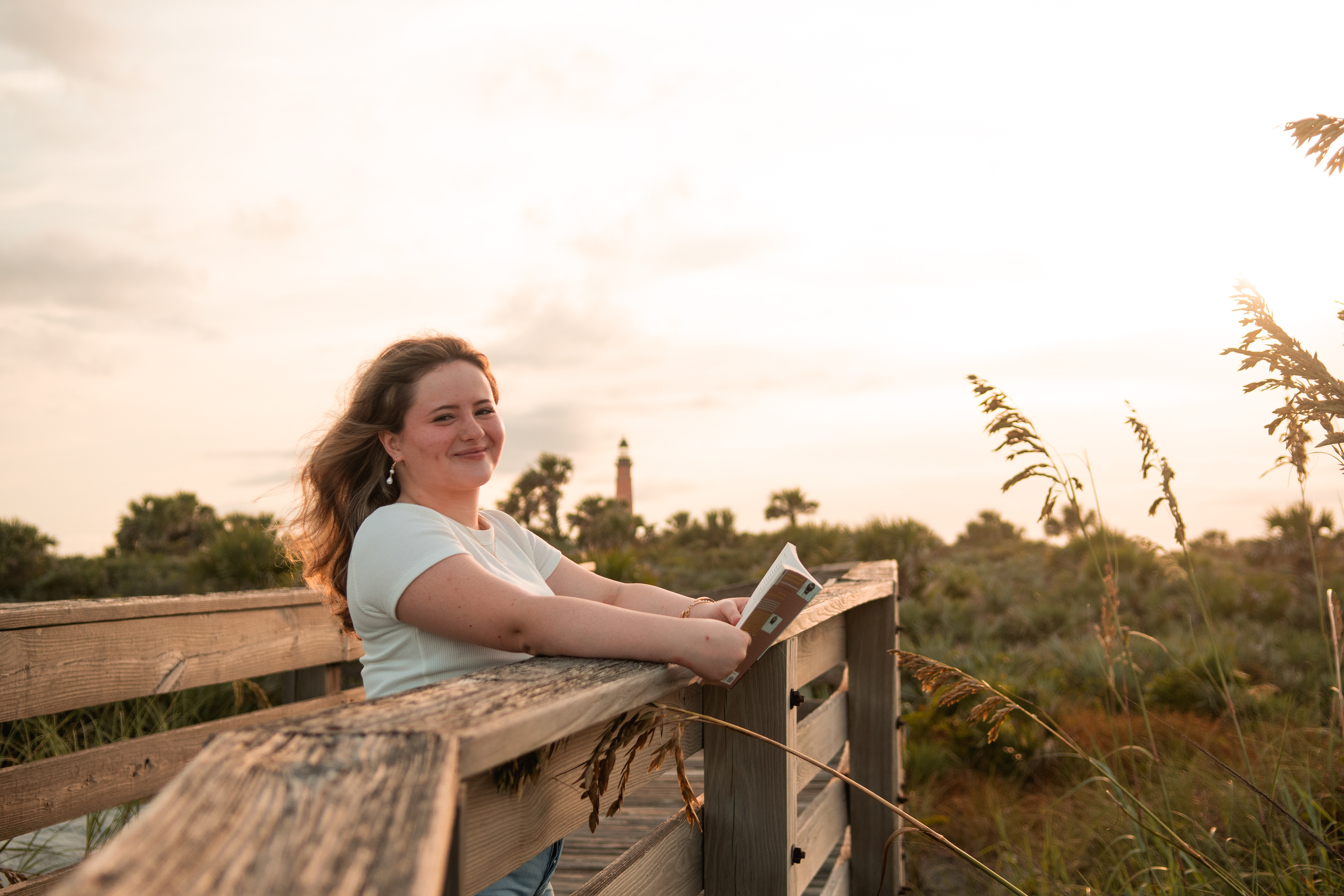 Senior portraits in Ponce Inlet FL, Nelly leaning casually on the boardwalk railing with the sun behind her.