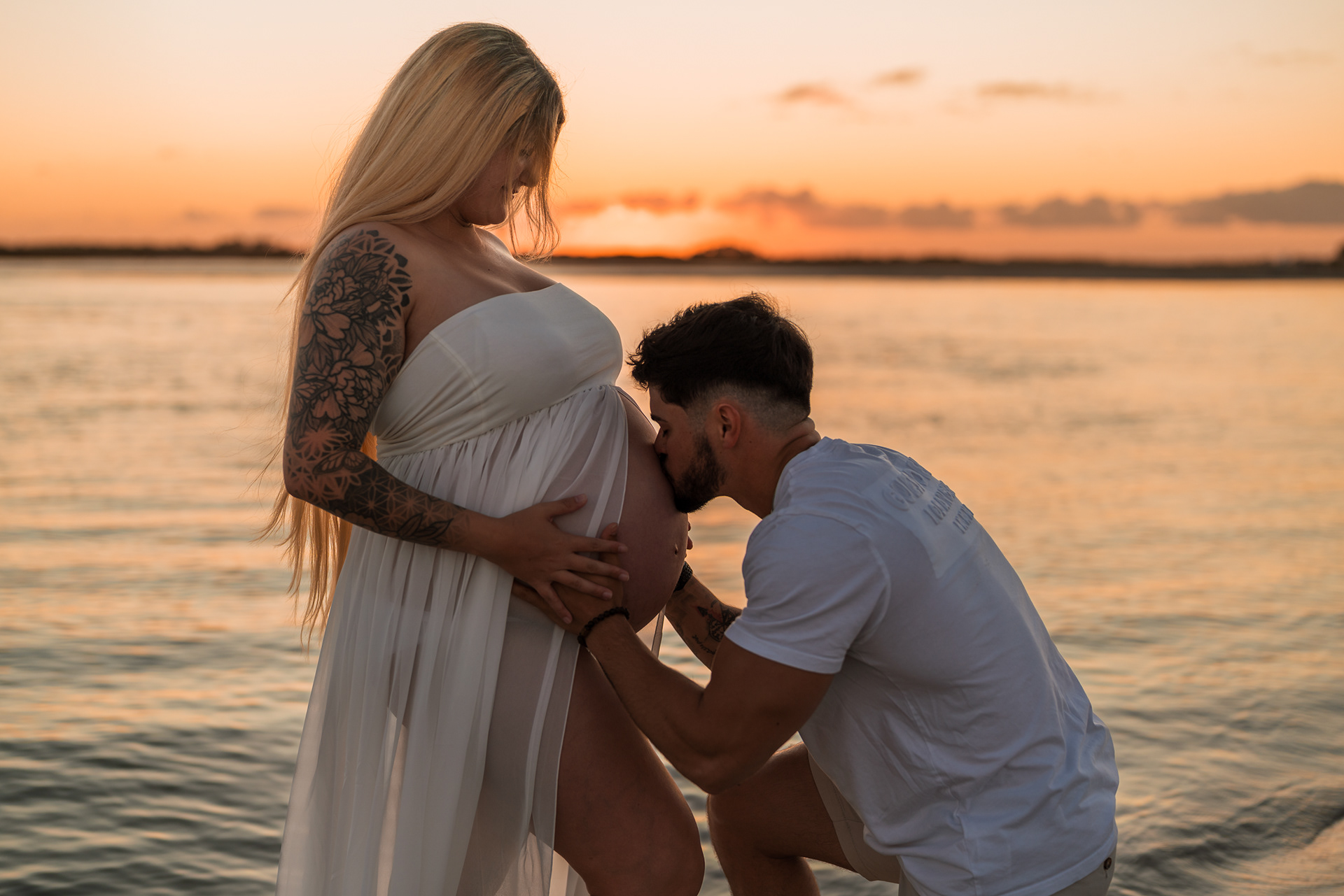 Close-up maternity photo of father kissing baby bump near the water