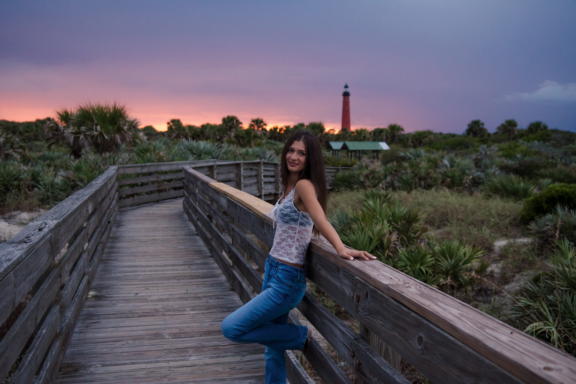 Senior portraits at Ponce Inlet Lighthouse, Mia leaning on the boardwalk railing with colorful sunset skies.