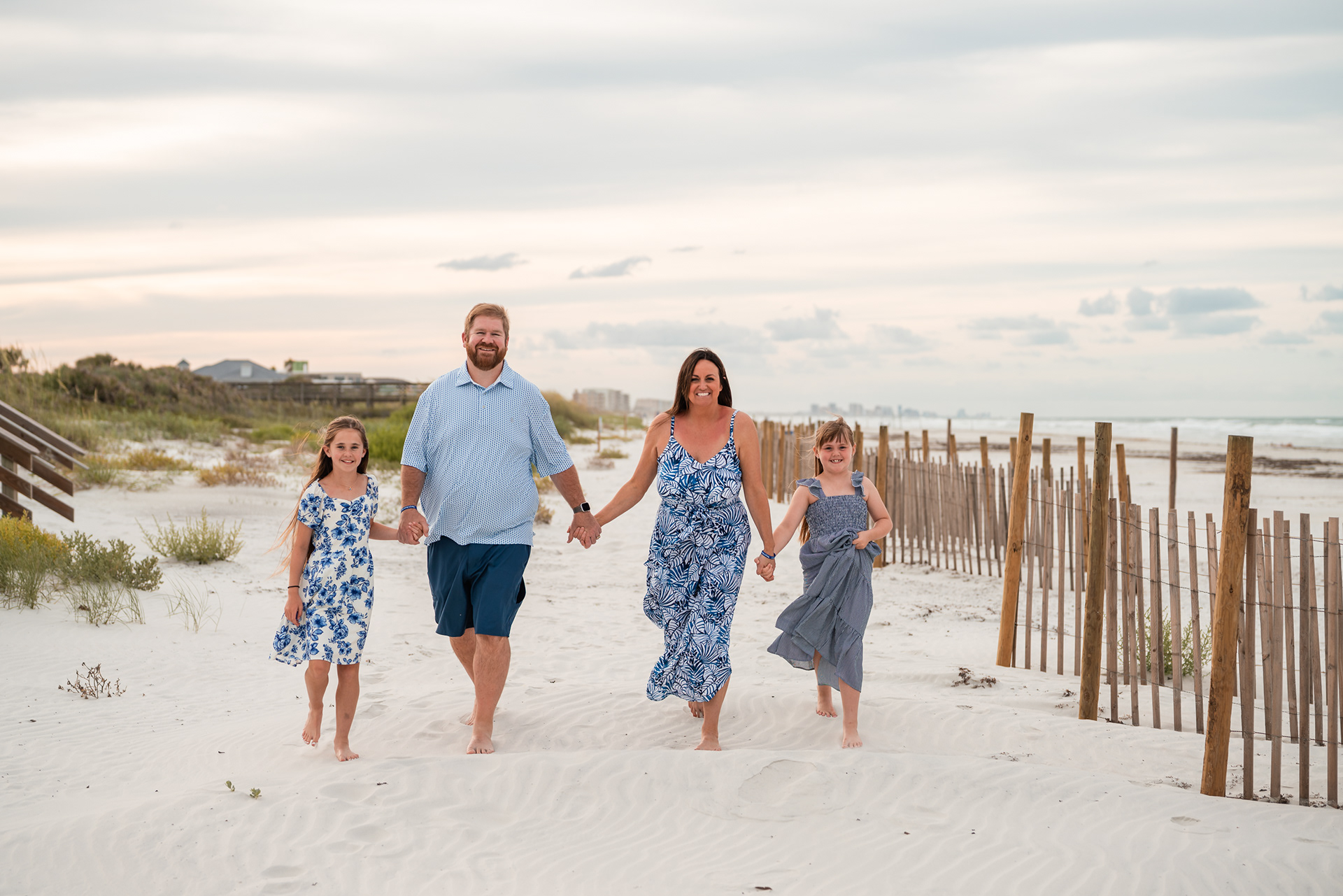 Family holding hands and walking through the dunes during a beach photo session in Ponce Inlet.