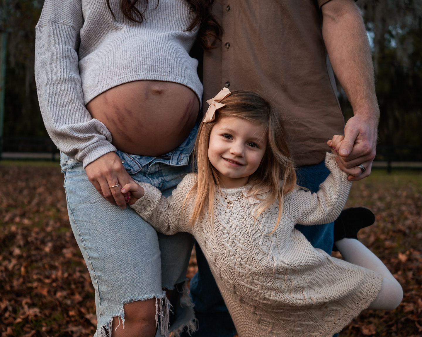 Family maternity photo with young child standing under parents and baby bump