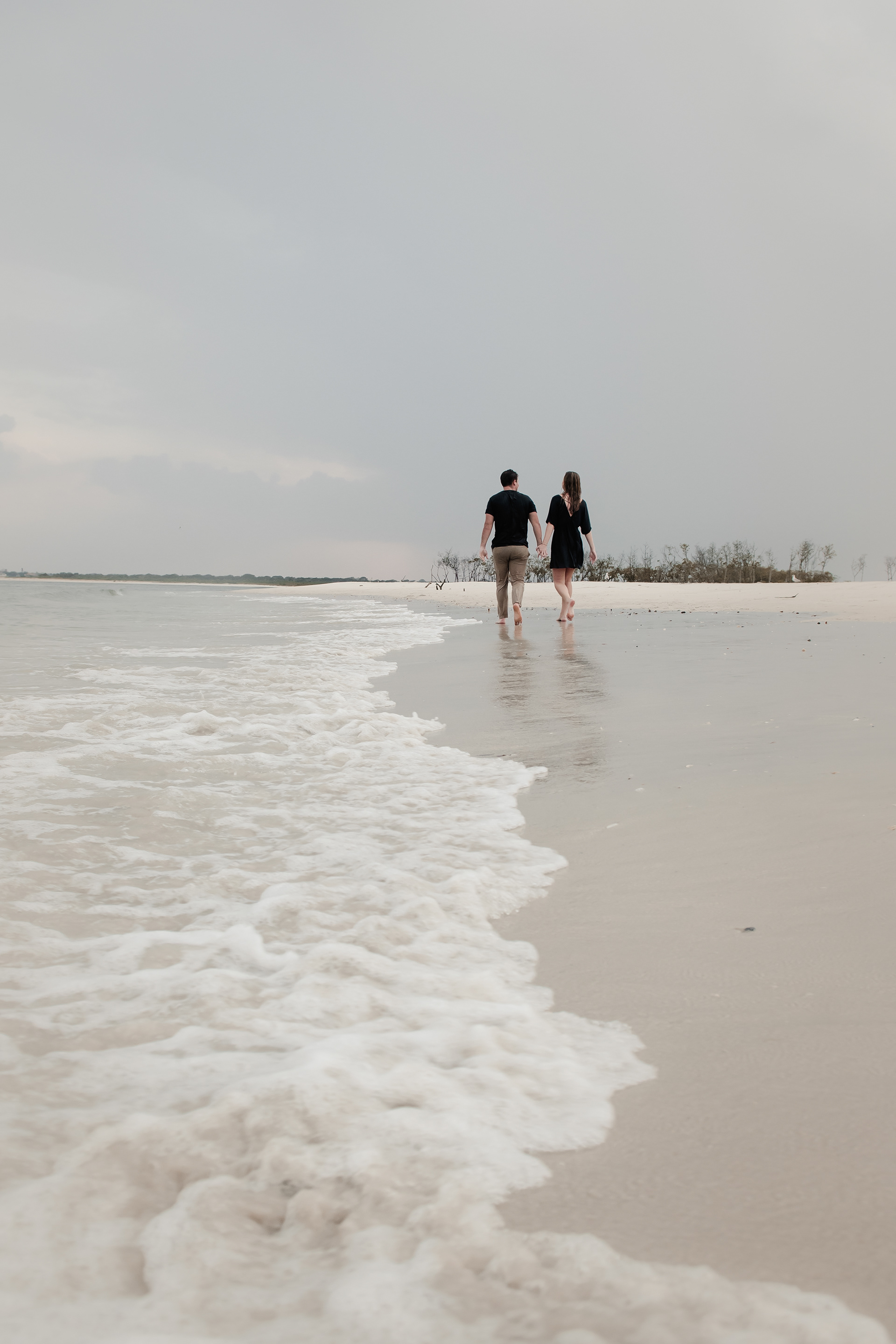 Couple walking along the shoreline during rainy engagement photos in Ponce Inlet Florida