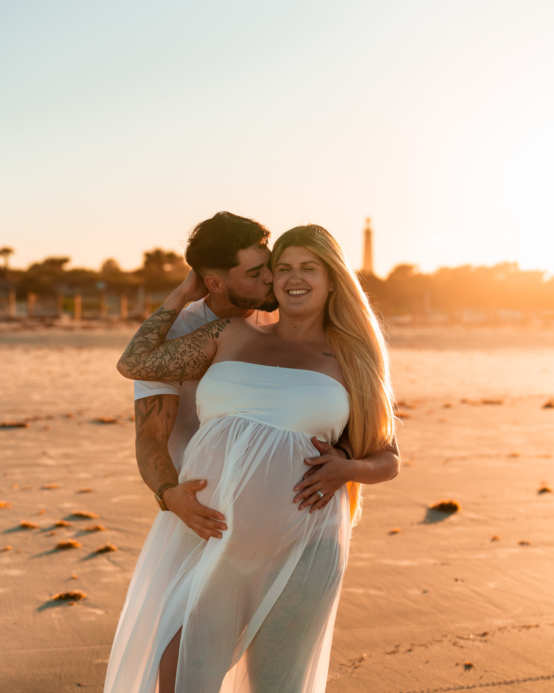 Couple maternity photo on the beach with parents walking together at sunset