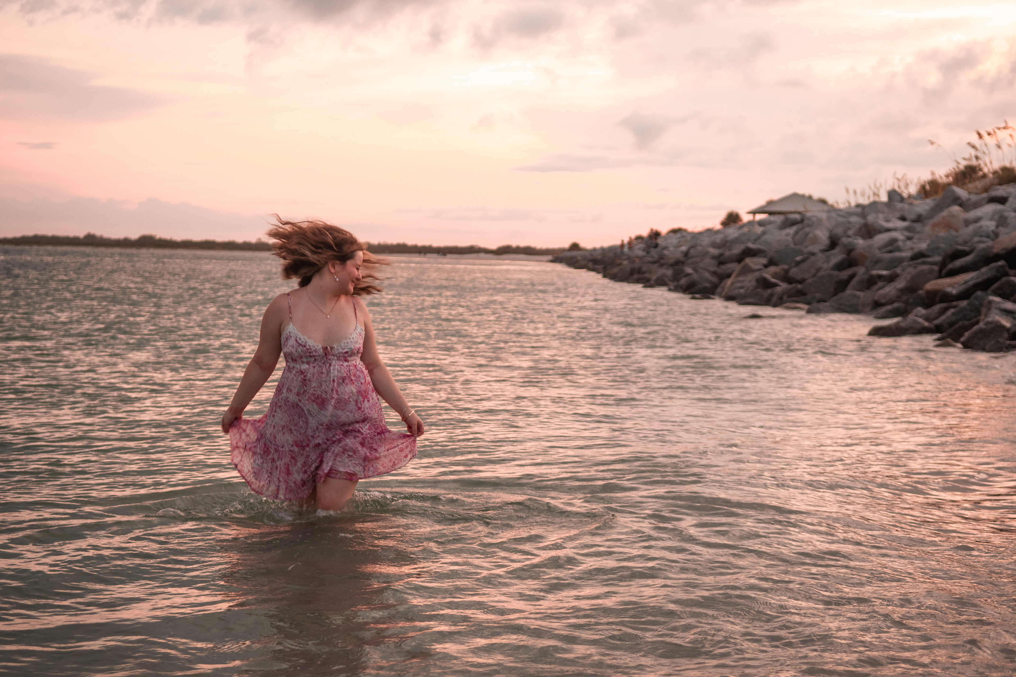 Senior portraits in Daytona Beach FL, Nelly holding her dress in the water with waves surrounding her.