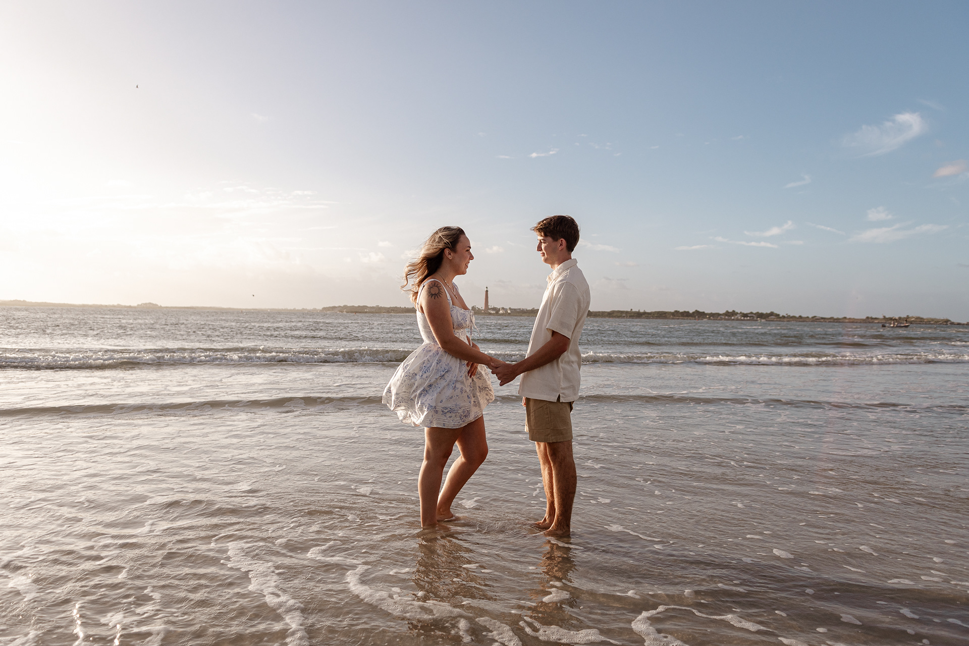 New Smyrna Beach engagement session, couple standing in the waves under a soft golden sky.