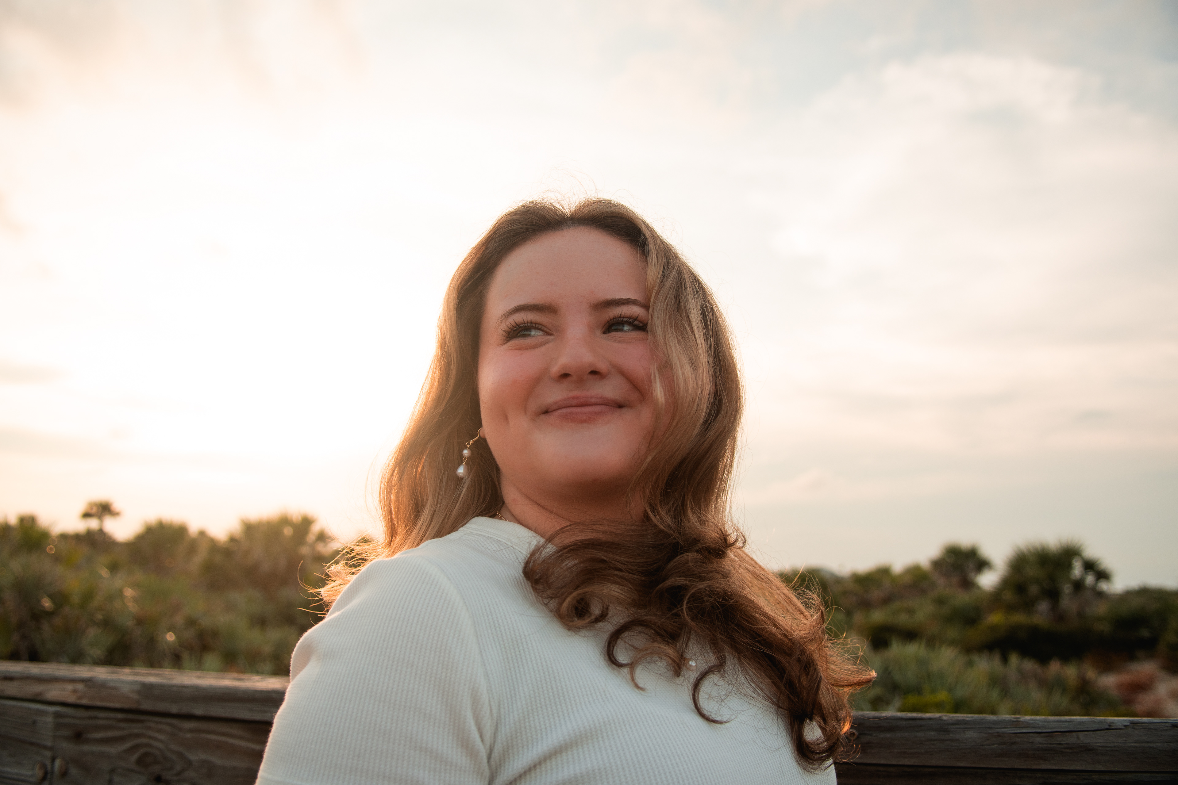 Close-up senior portrait in Ponce Inlet, Nelly looking off camera with golden sun lighting her hair.