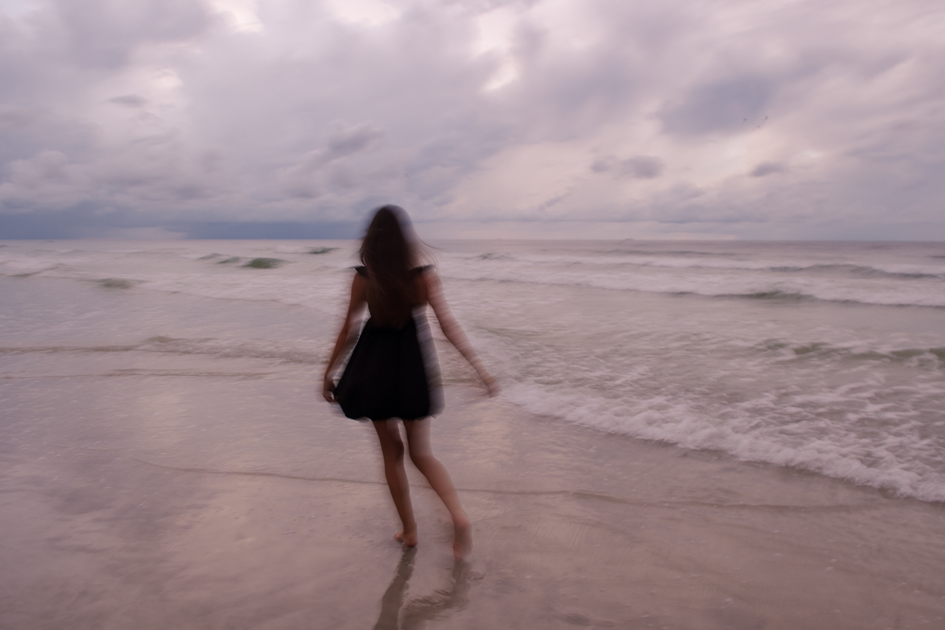 Artistic senior photo at Ponce Inlet with blurred motion of Mia walking into the ocean waves at sunset.