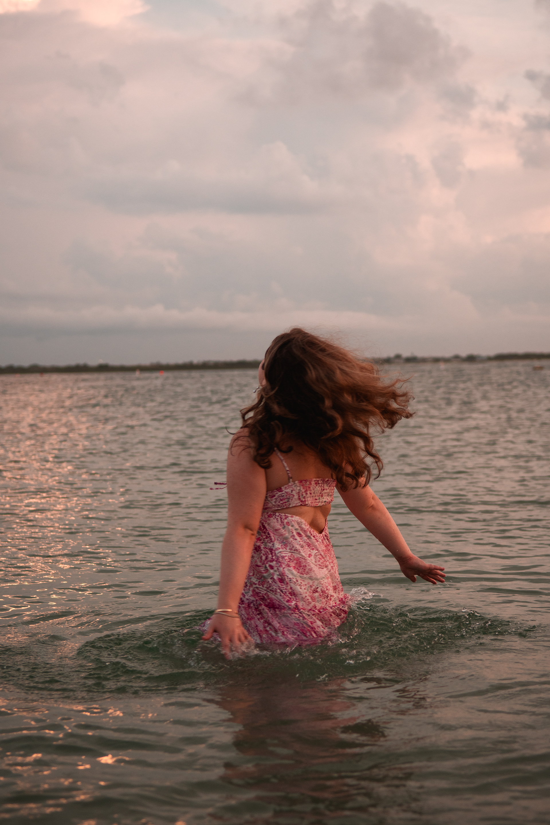 Ponce Inlet senior photo session, Nelly standing ankle-deep in inlet water, hair blowing in the wind.