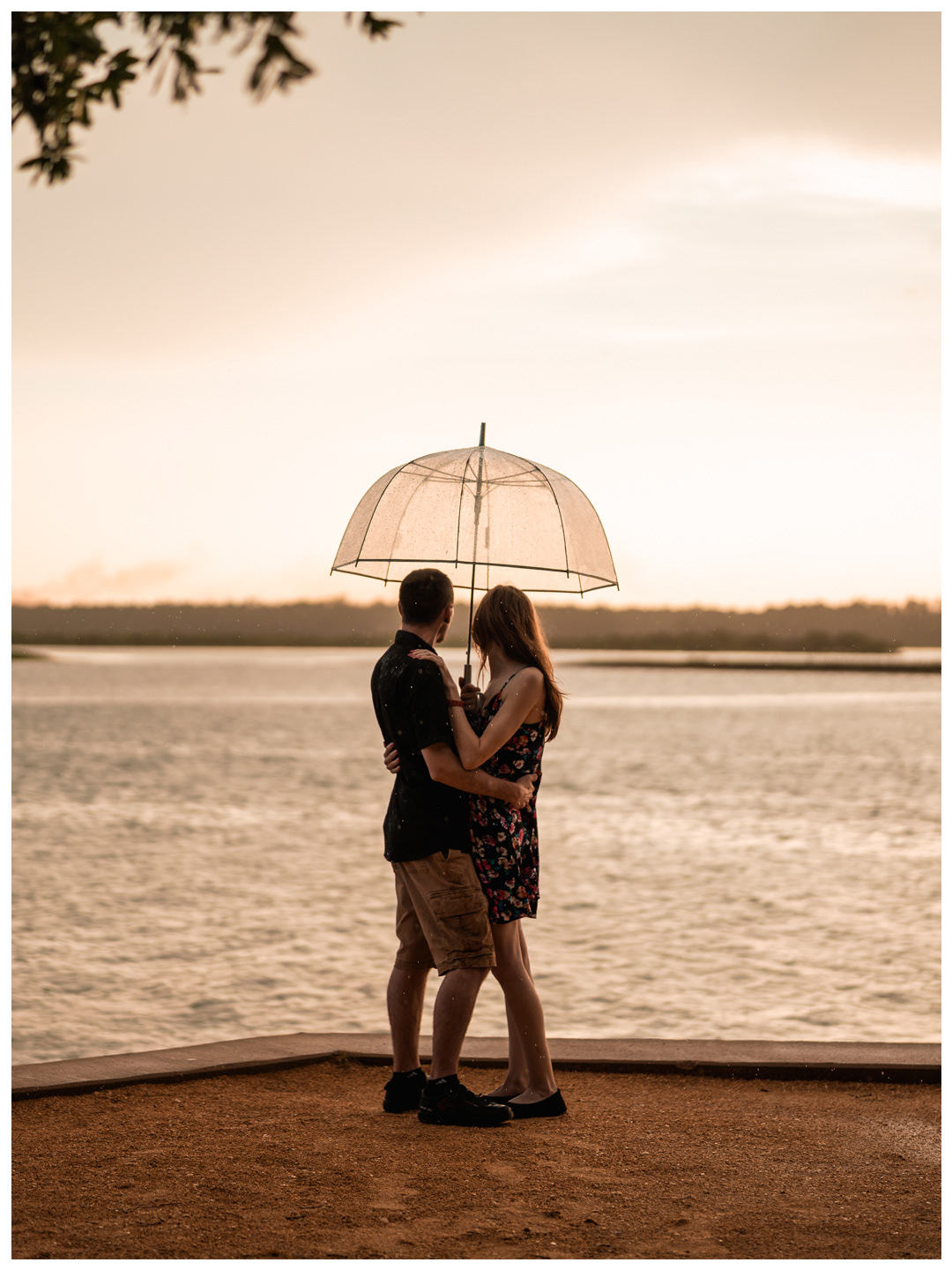 Wide portrait of a couple embracing beneath an umbrella beside the river at Washington Oaks Gardens State Park.