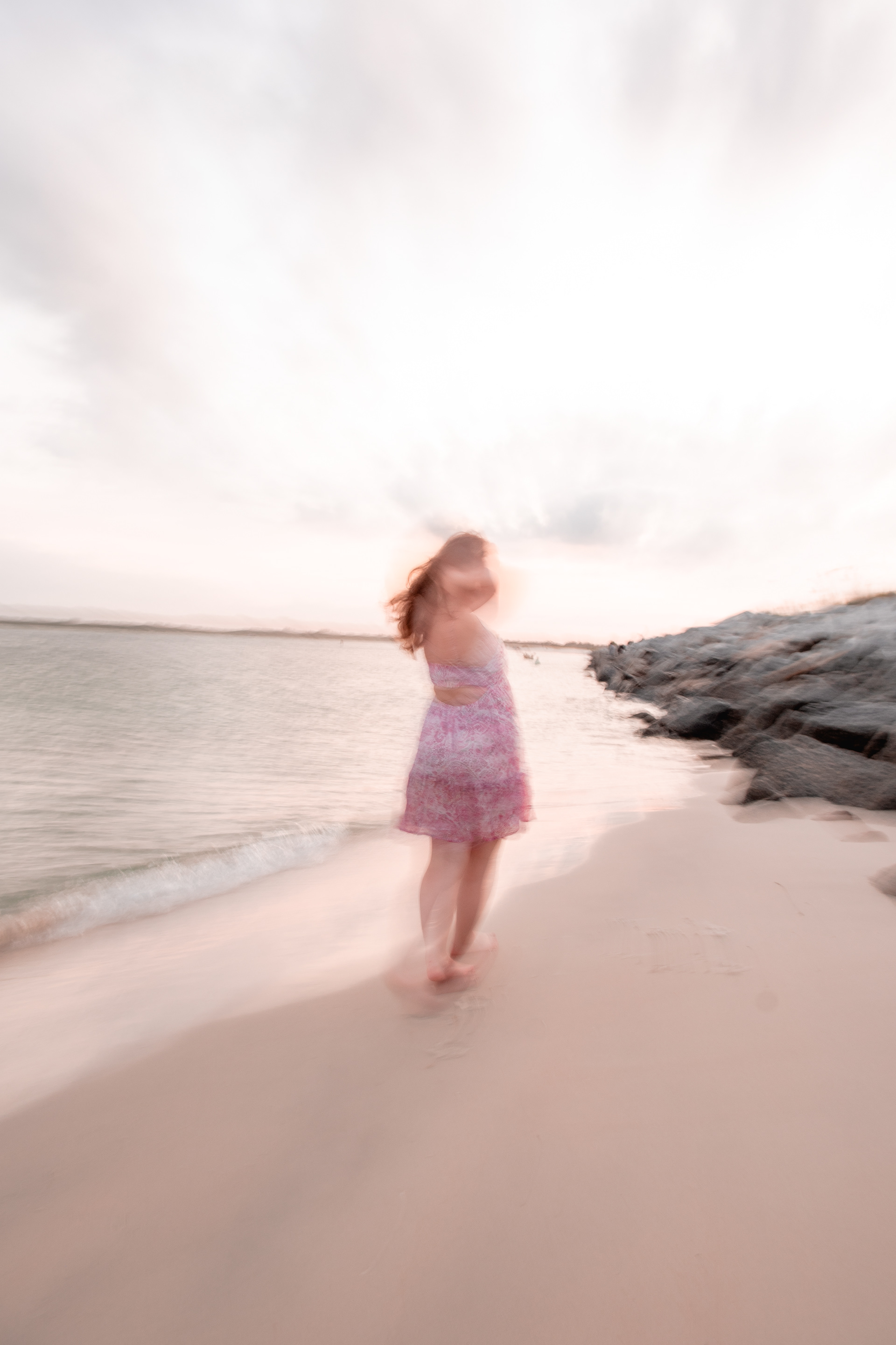 Creative blurred motion senior portrait at Ponce Inlet Beach, Nelly in pink dress walking along shoreline.