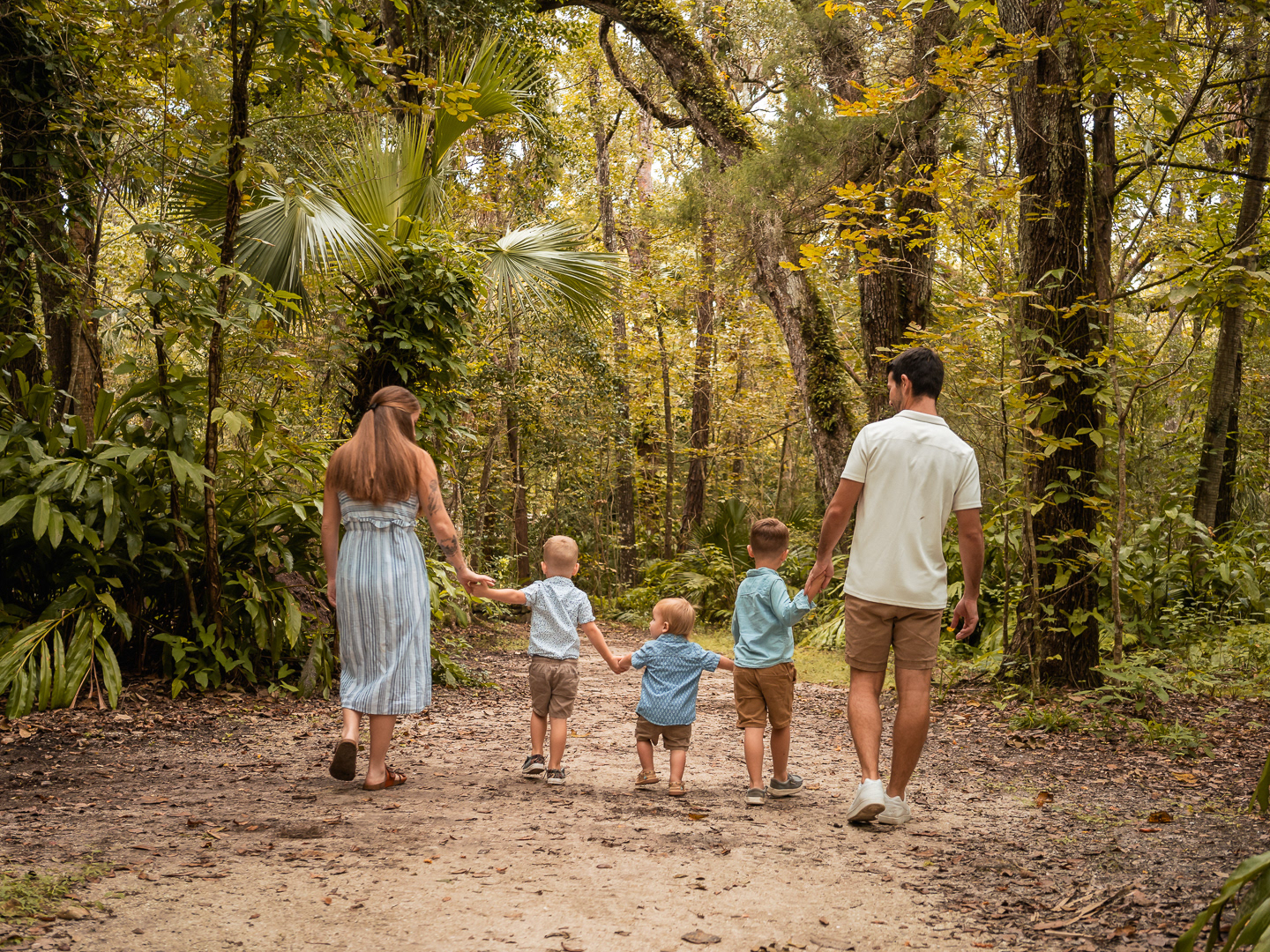 Family walking hand in hand down a tree-lined path at Dunlawton Sugar Mill Gardens during Port Orange family session.