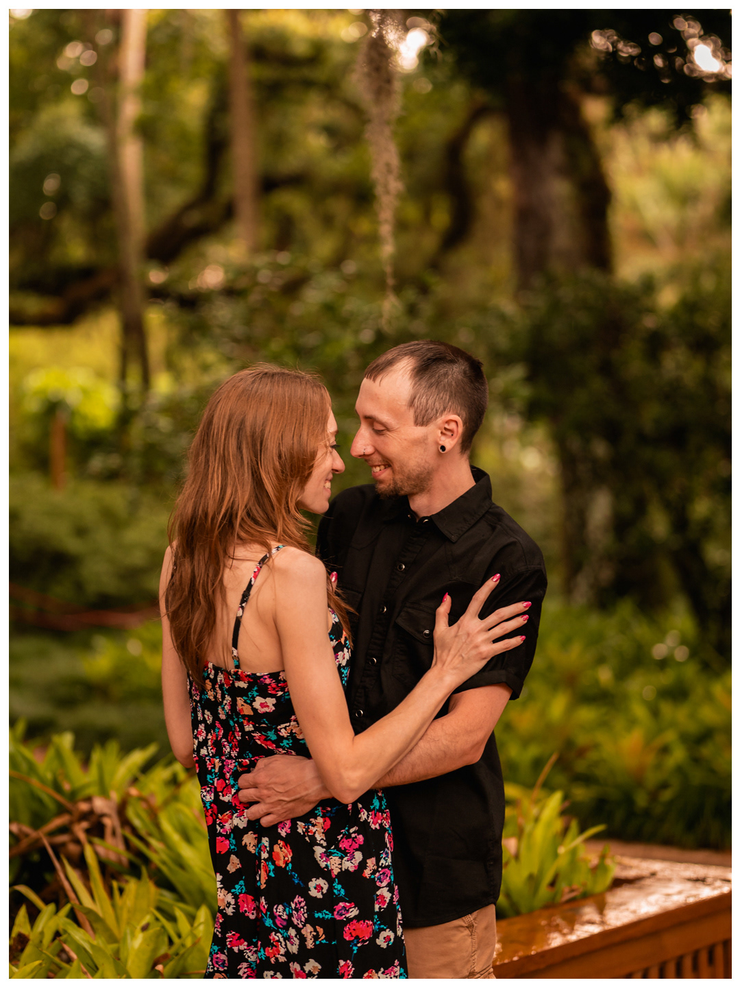 Couple smiling and embracing near a wooden railing in the gardens at Washington Oaks.
