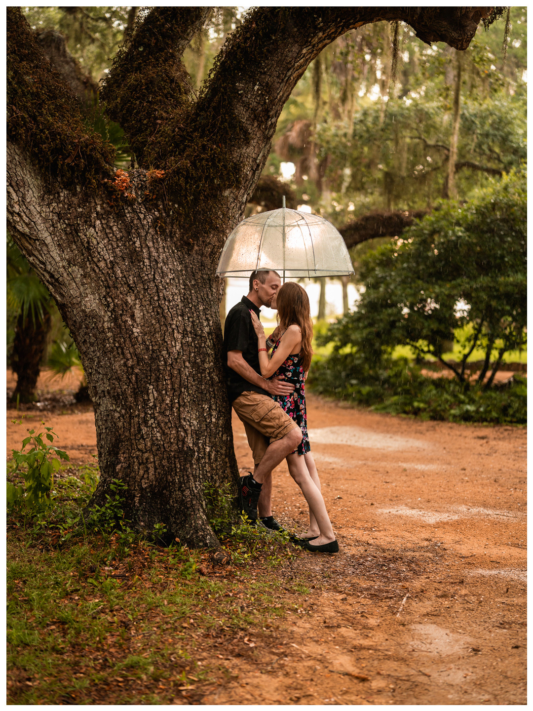 Wide portrait of a couple leaning against a large oak tree during a rainy Washington Oaks Gardens photo session.