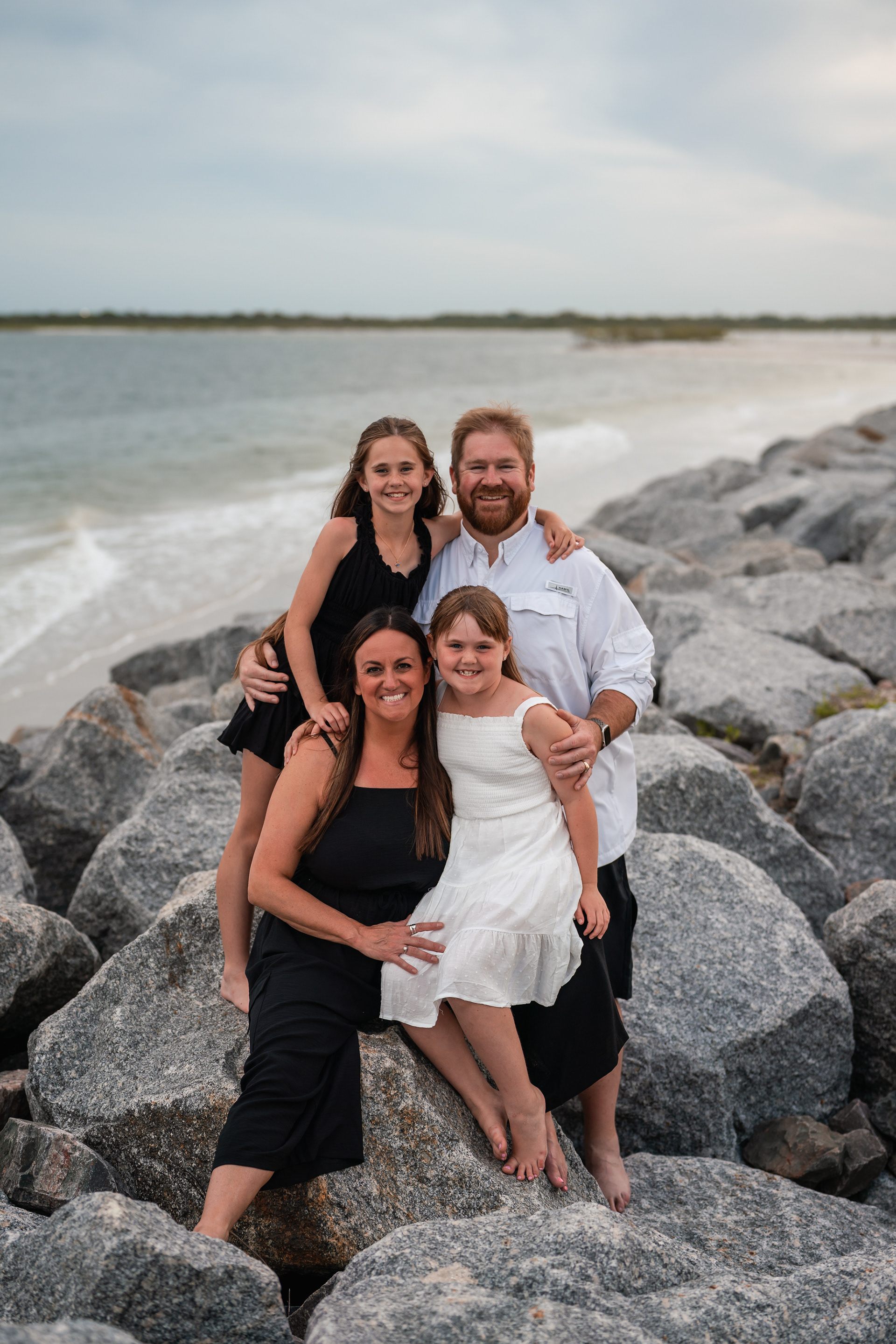 Family portrait on the rocks by the water during a beach photography session in Ponce Inlet.