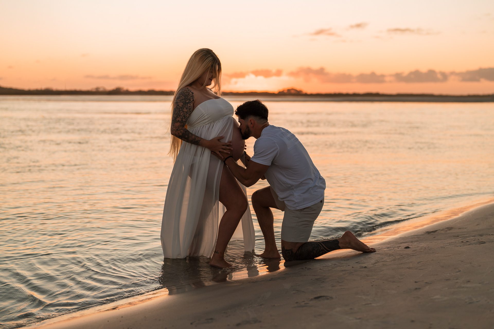 Father kneeling by baby bump during beach maternity photos in Florida