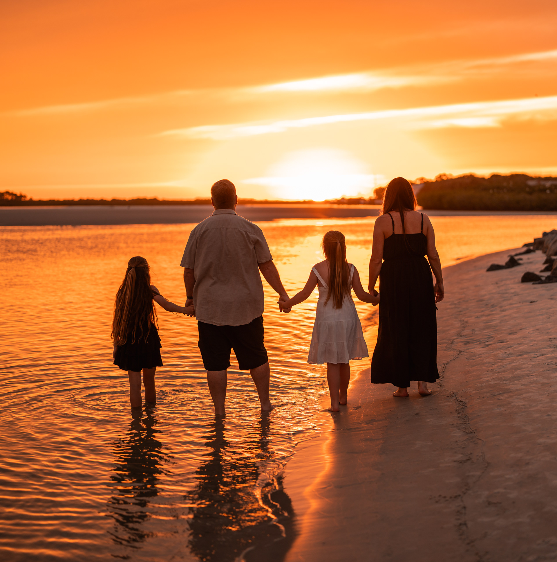 Family standing together in the water at sunset during a Ponce Inlet beach family photo session.