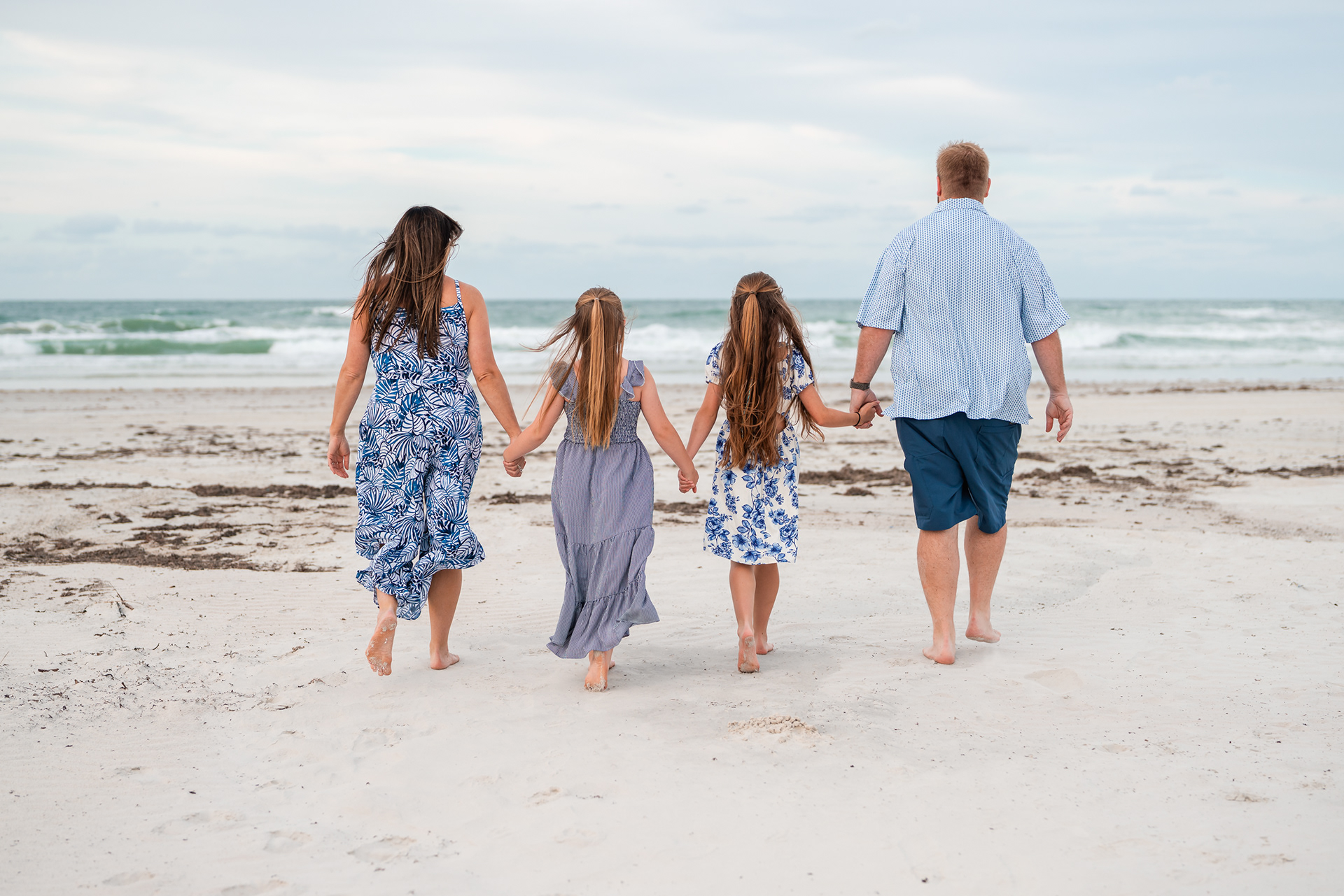 Family walking toward the ocean during a beach photography session in Ponce Inlet.