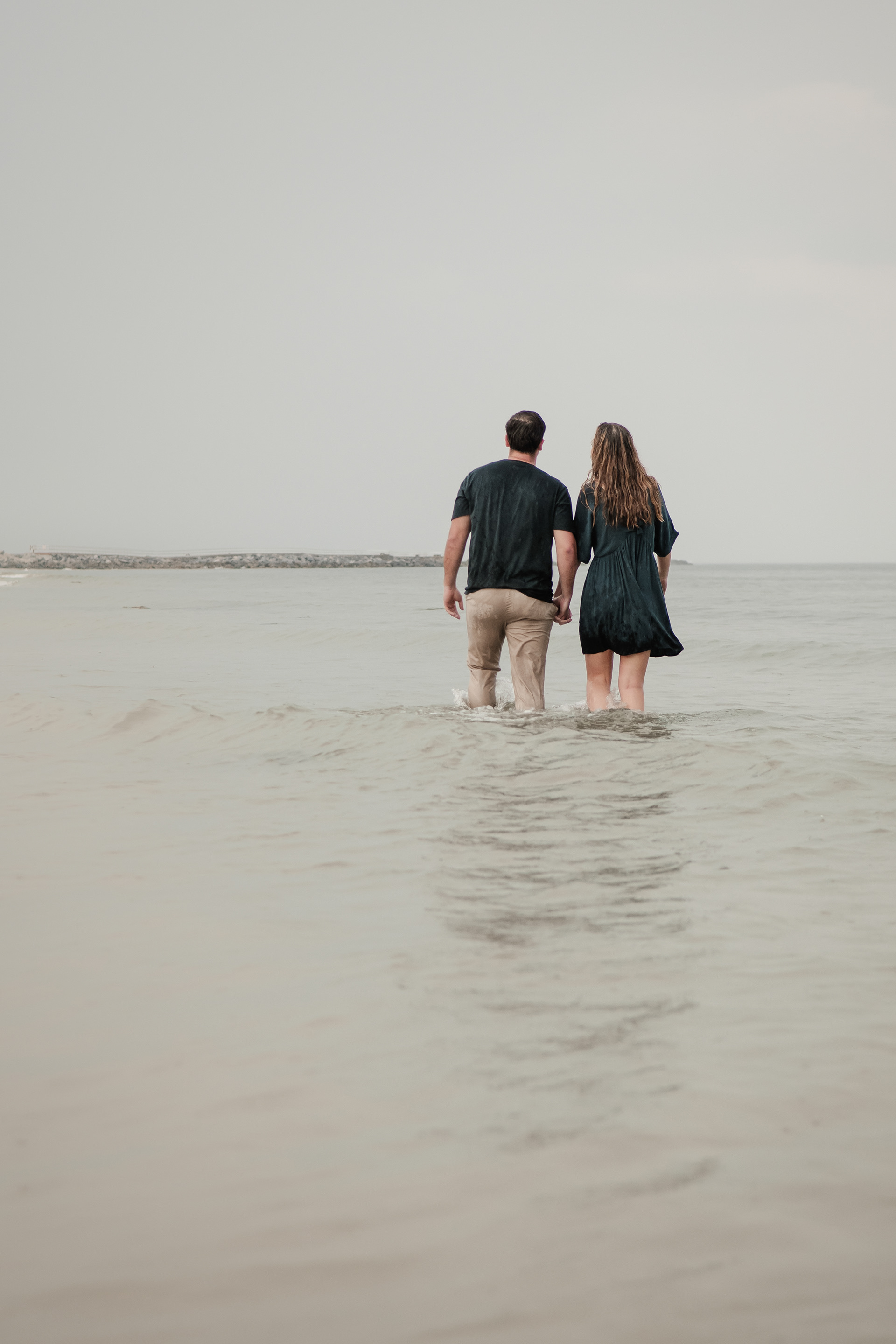 Couple standing in shallow water during Ponce Inlet engagement photos on a rainy beach