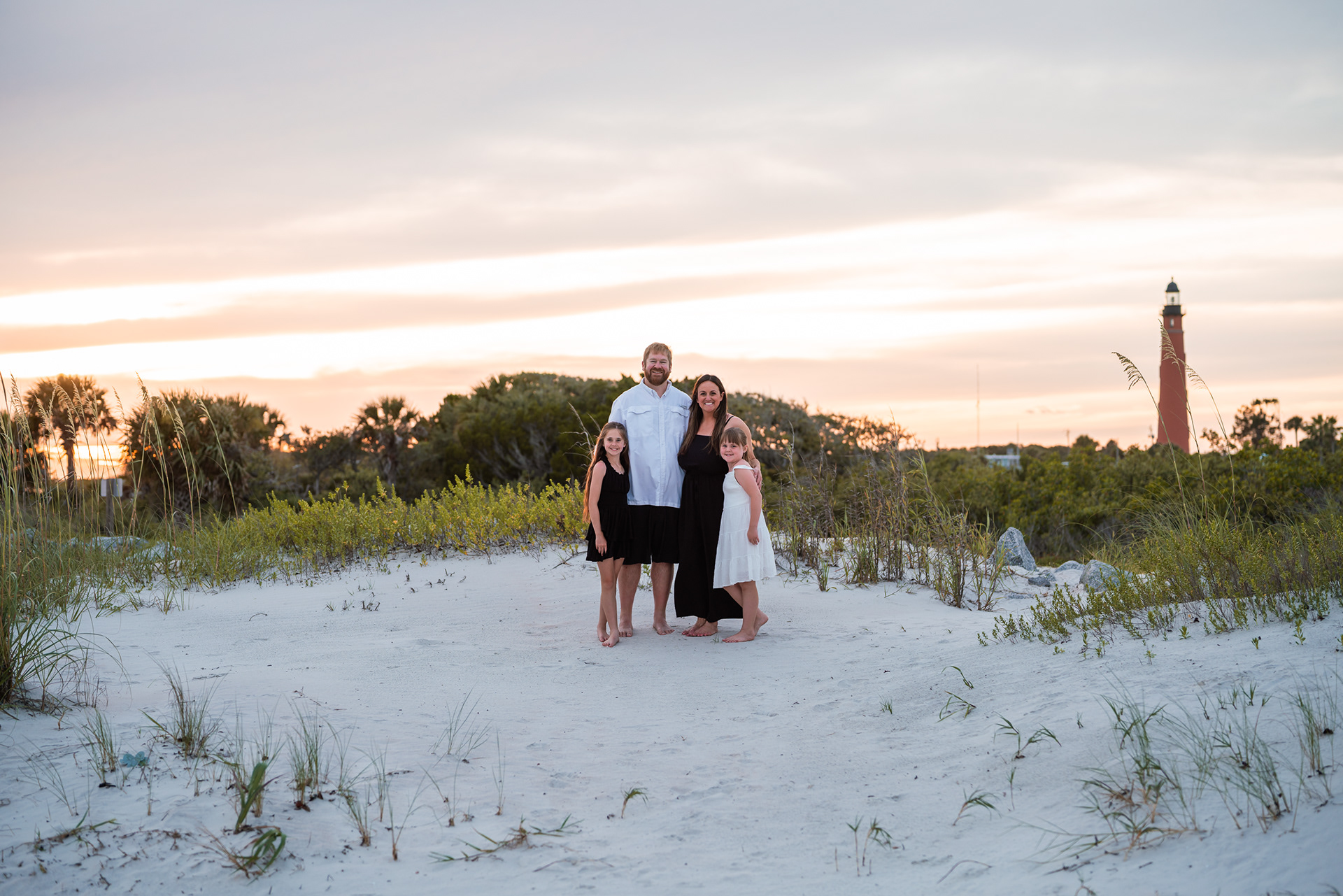 Family standing in the dunes near Ponce Inlet Lighthouse during a beach photo session.